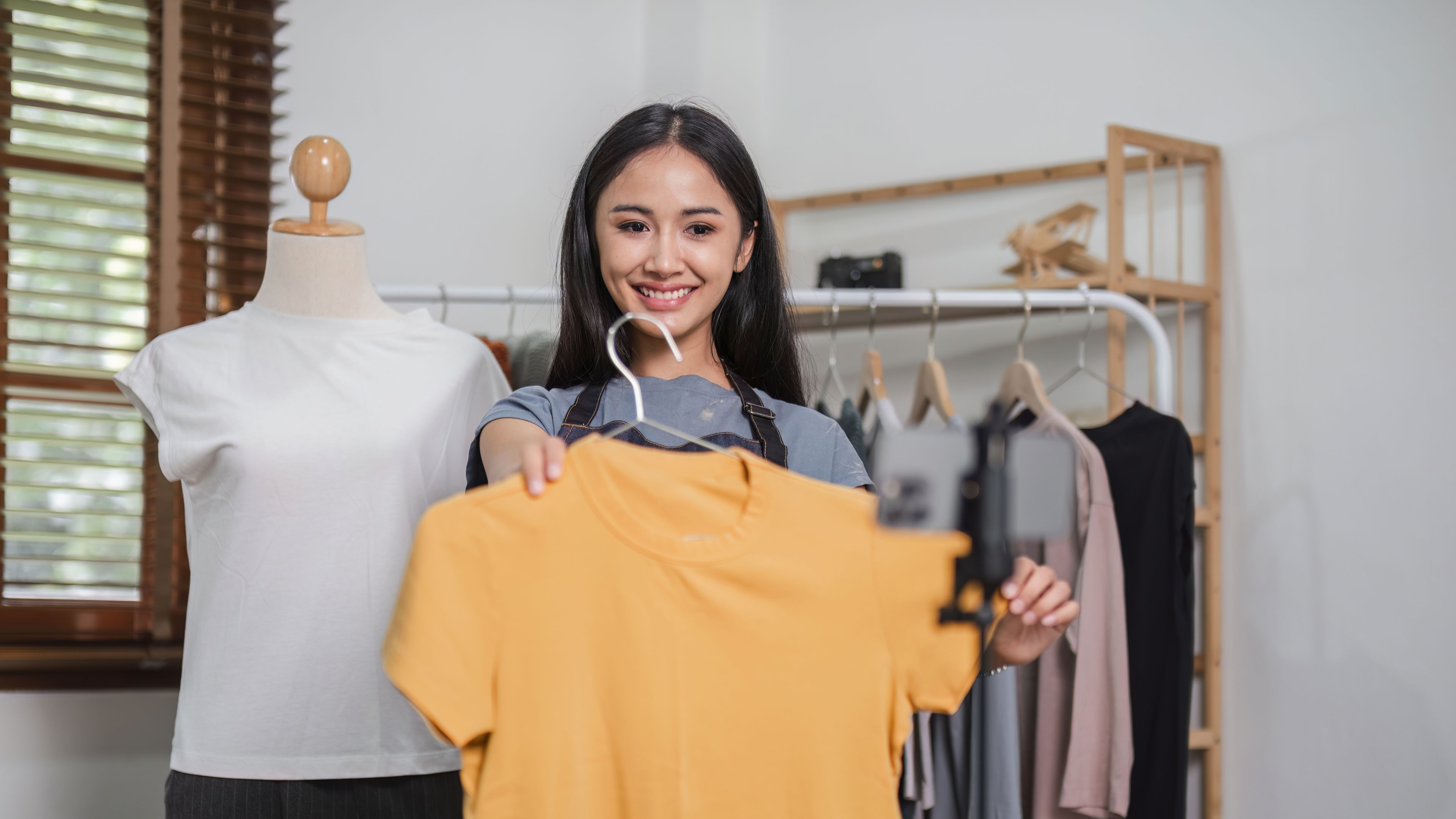 Asian woman holding a yellow dress in hand in a clothing shop.