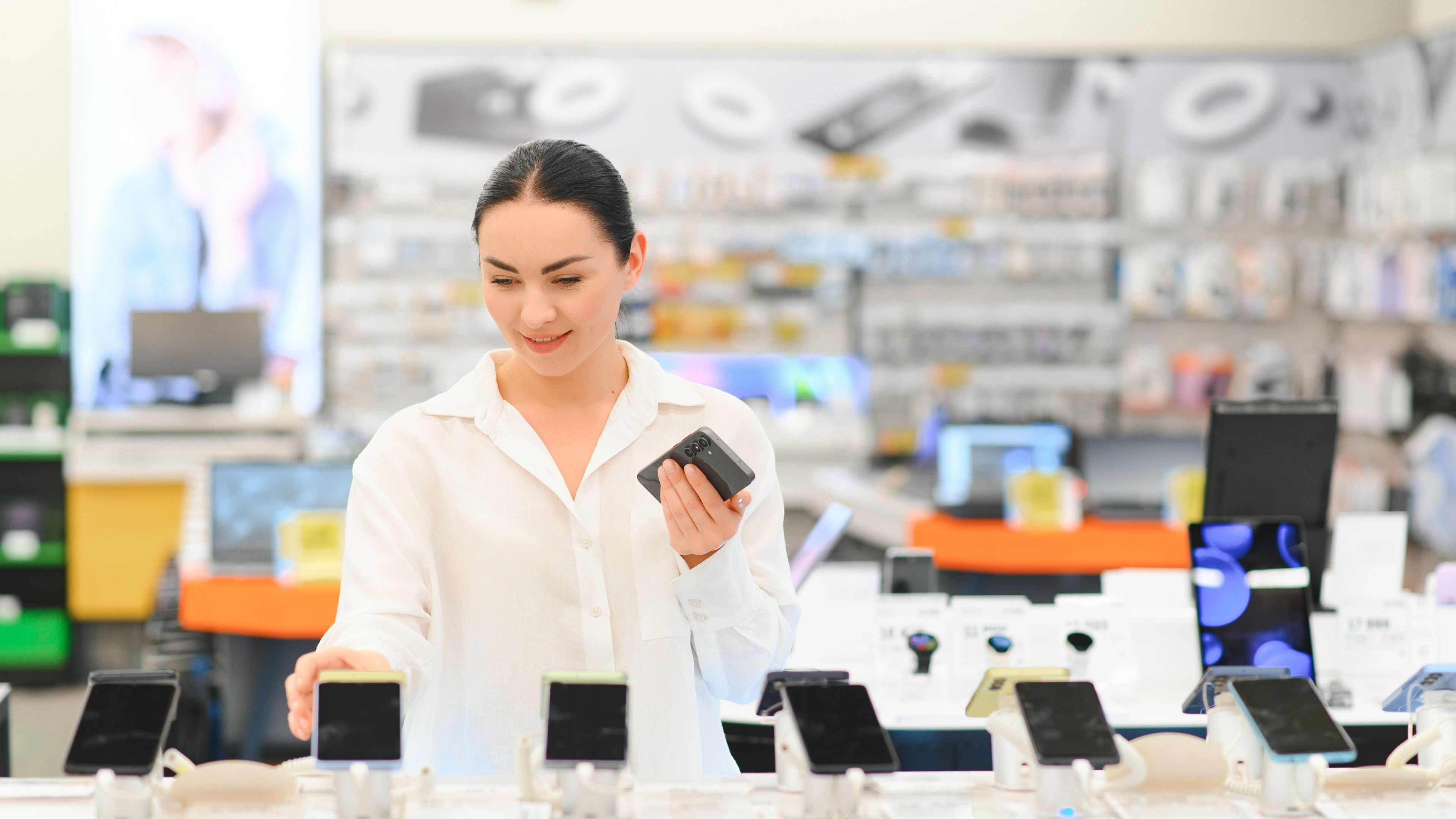 A happy woman looking and smiling with a new smartphone in hand in a gadget shop 