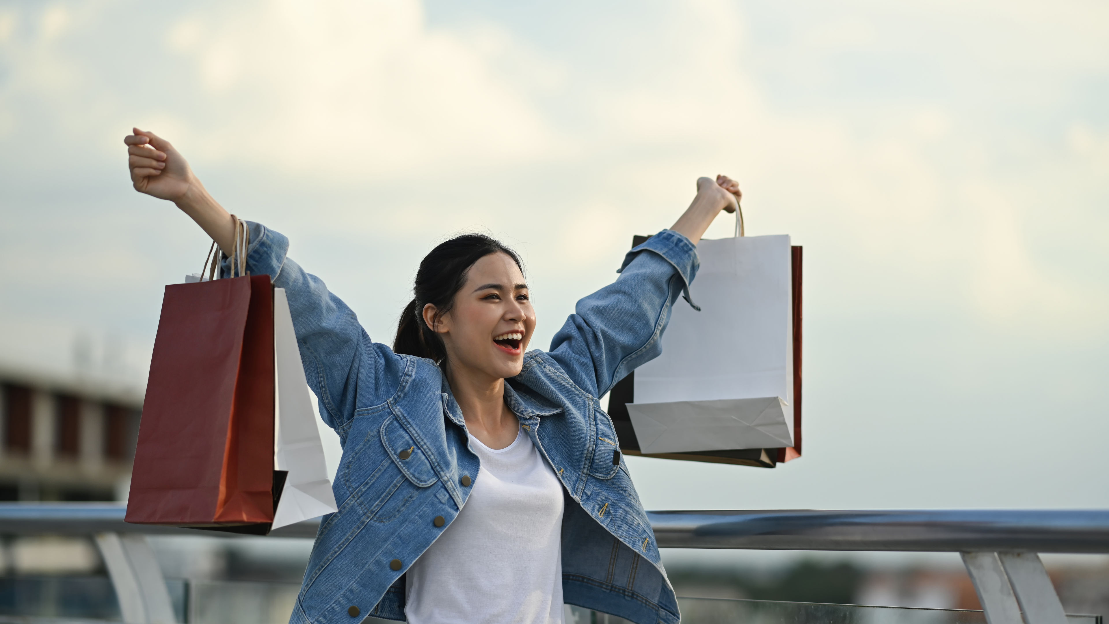 Overjoyed woman holding shopping bags nakatayo laban sa cityscape sa paglubog ng araw sa background 