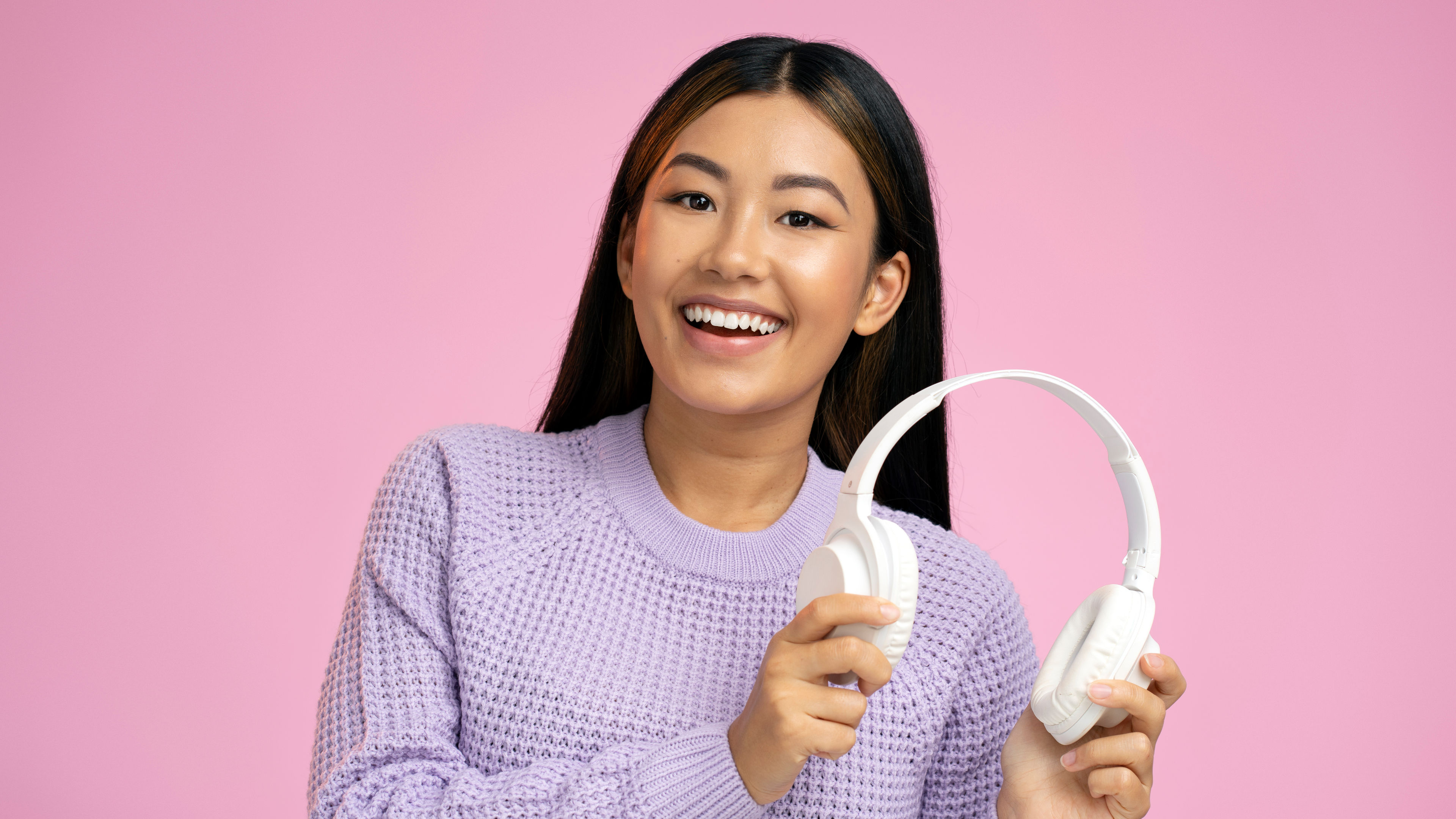 Studio portrait of relaxed cheerful asian woman holding wireless headphones 