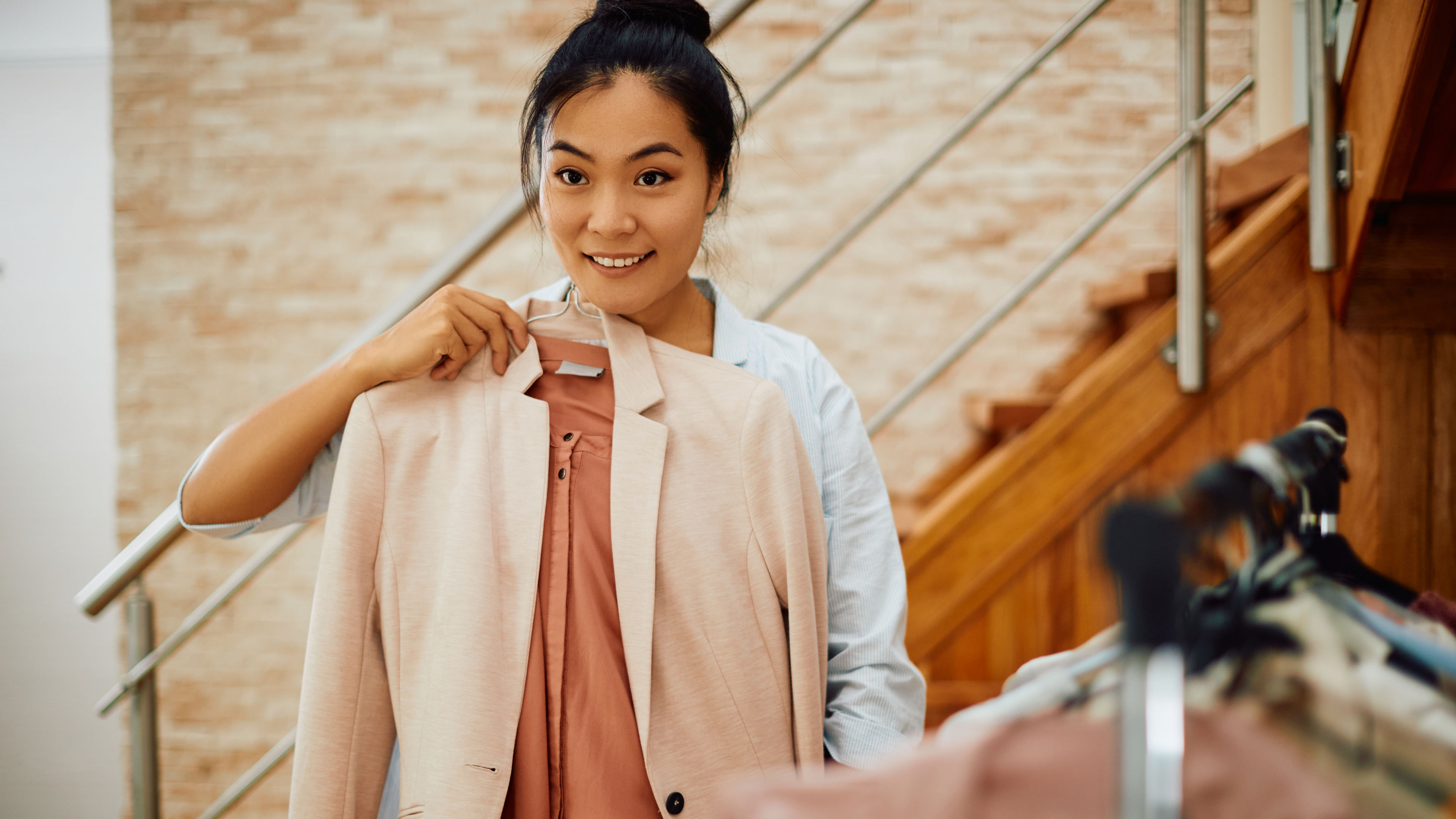 Young Asian woman holding hanger with her clothes while choosing what to wear