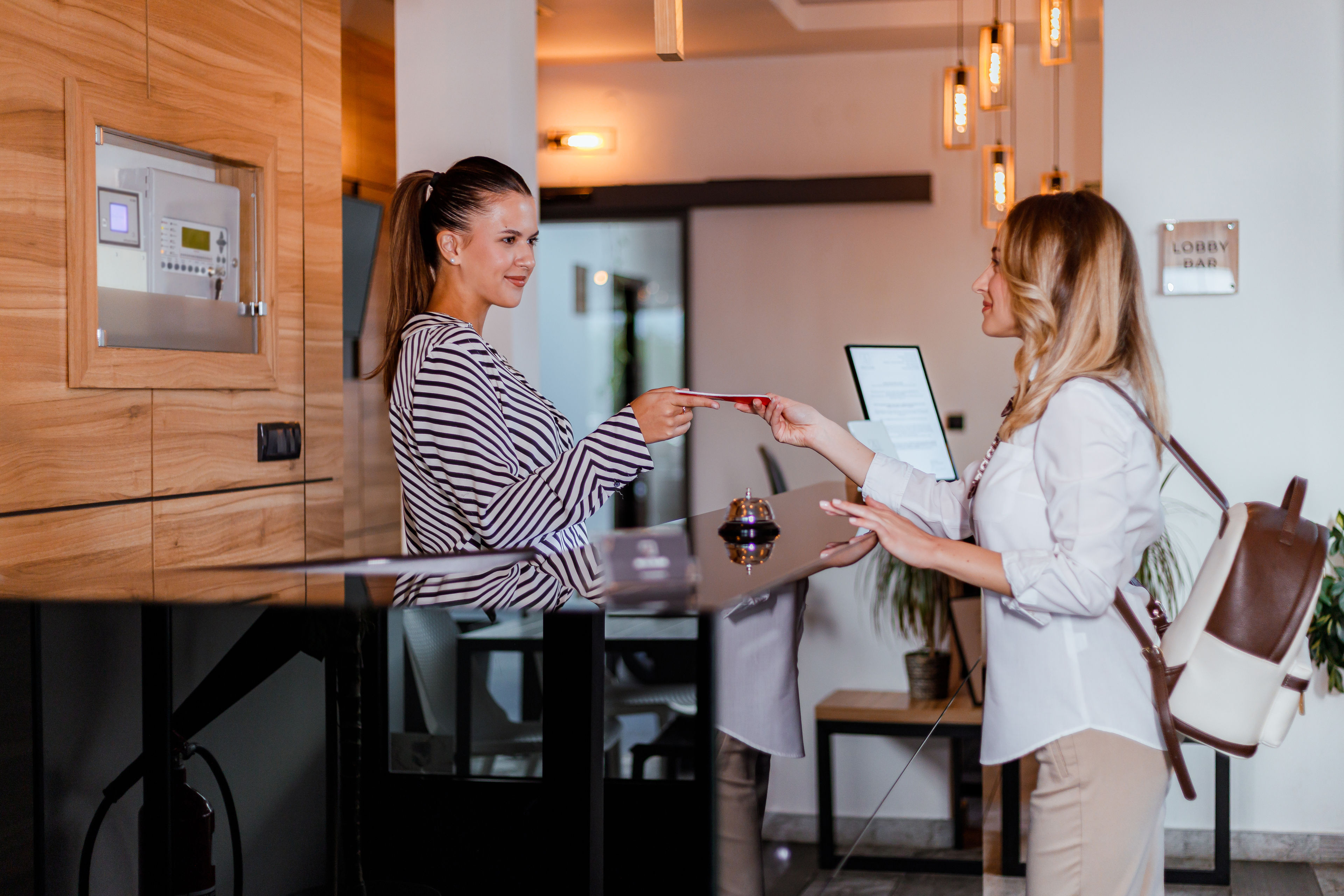 A hotel receptionist helps guests check in and provides a room access card in a modern lobby setting