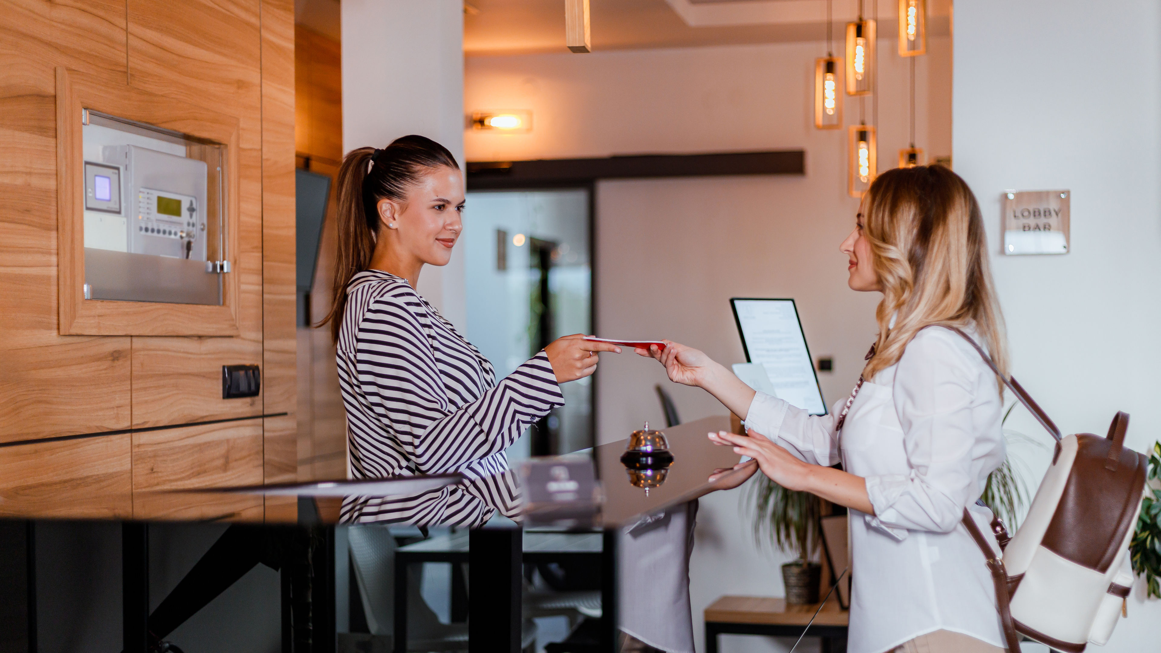 A hotel receptionist helps guests check in and provides a room access card in a modern lobby setting