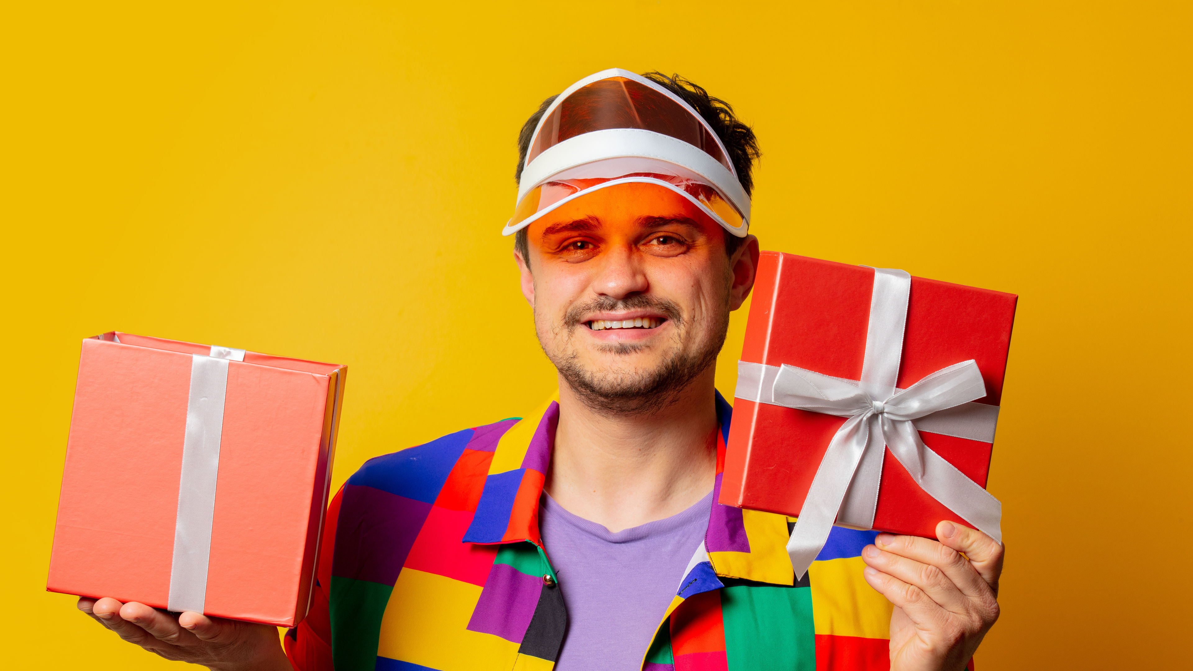 A stylish guy in colourfull dress holding 2 gifts in hand