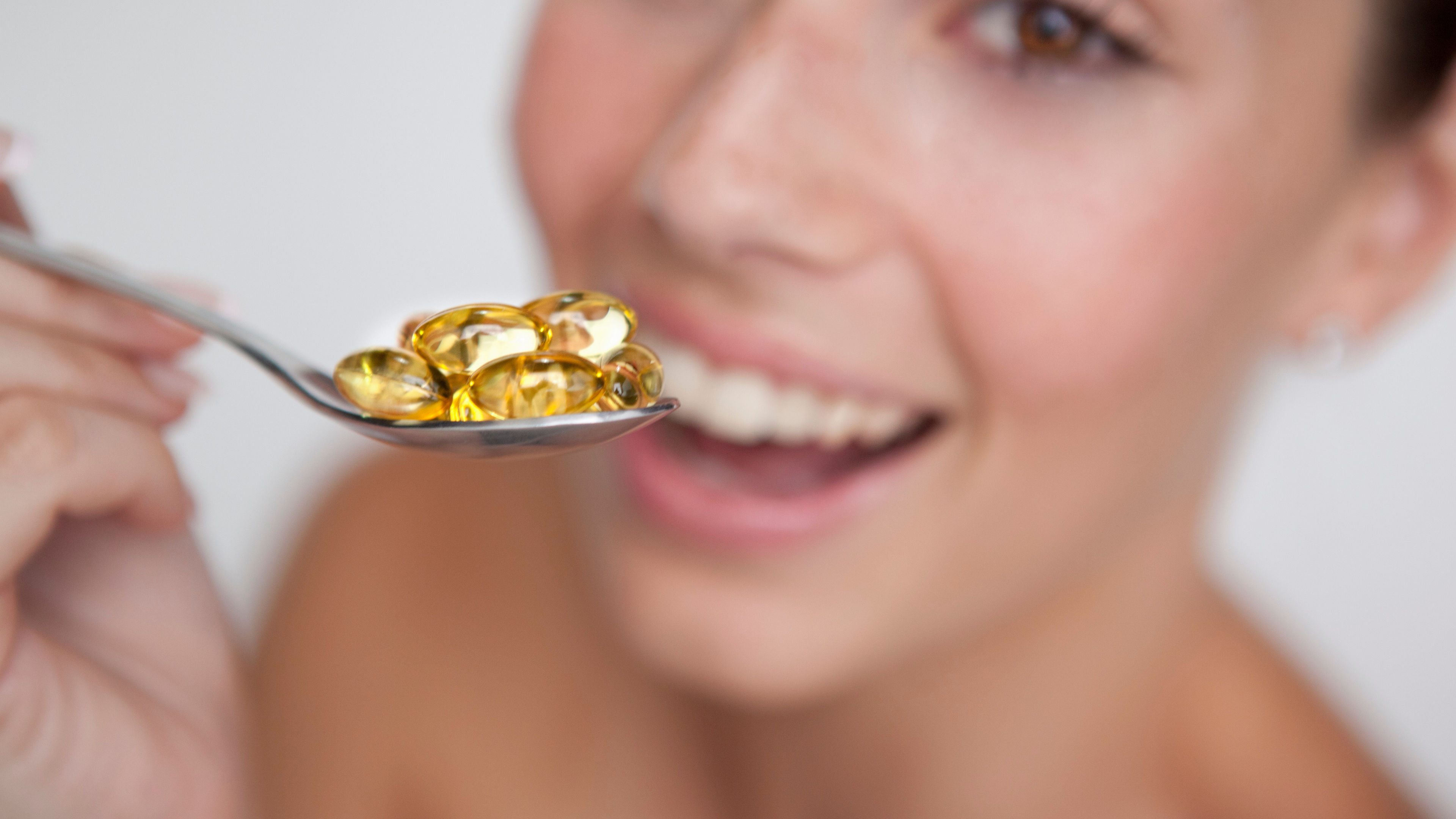 Woman Smiling with Spoonful of Golden Capsules 