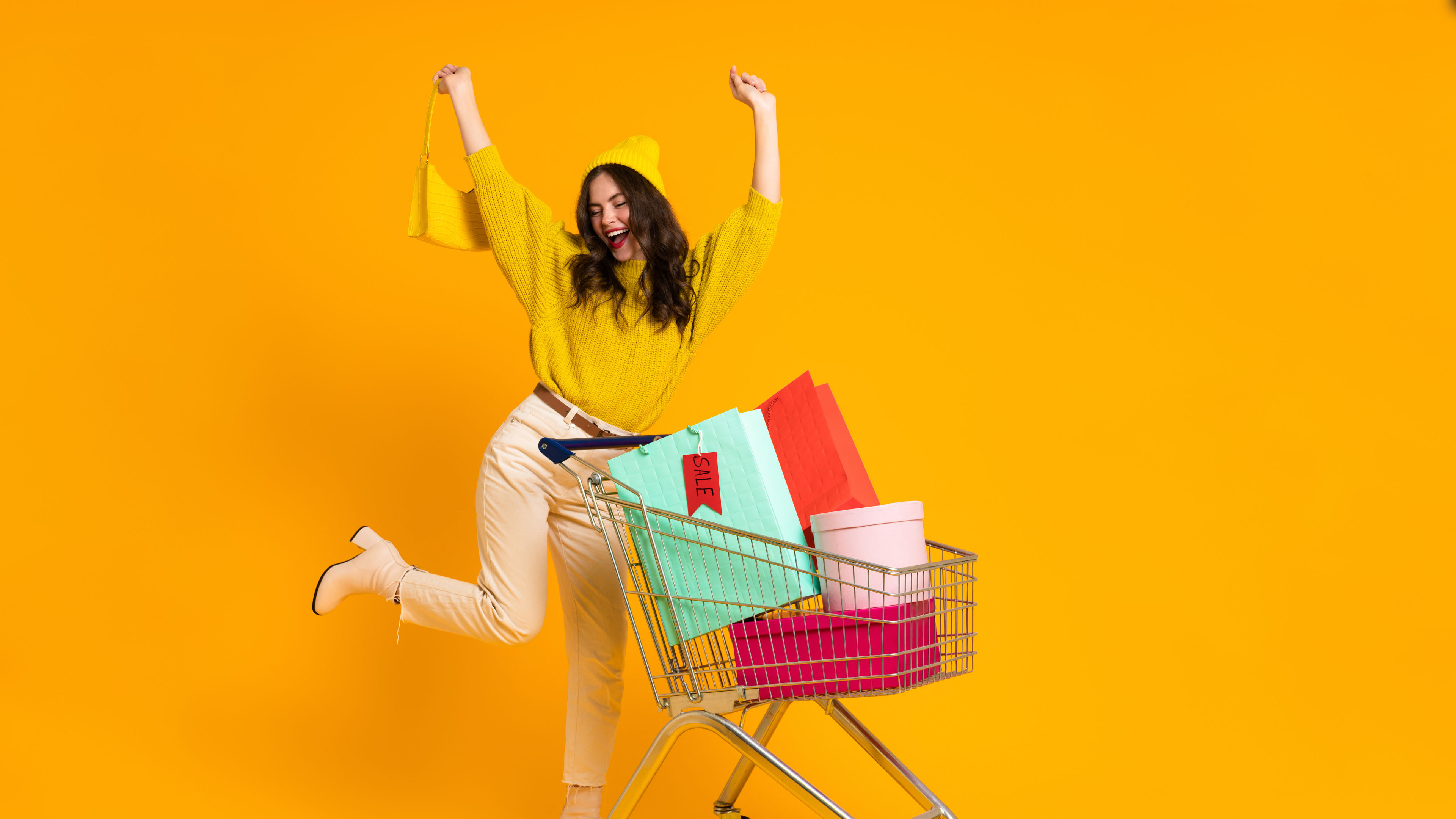 White woman making winner gesture while posing with shopping cart