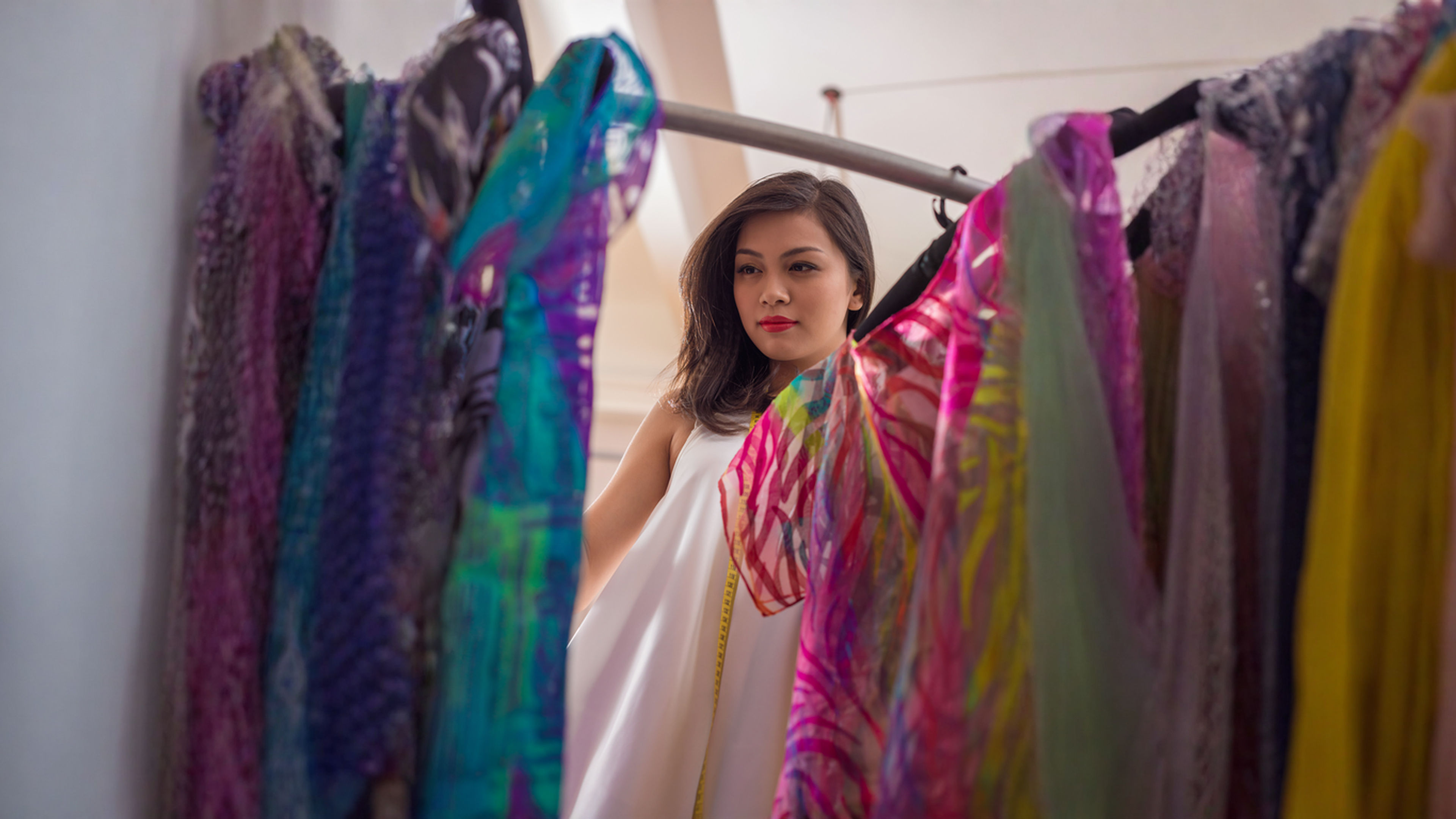 A good looking Asian woman in white dress checking colorful clothes in a rack.