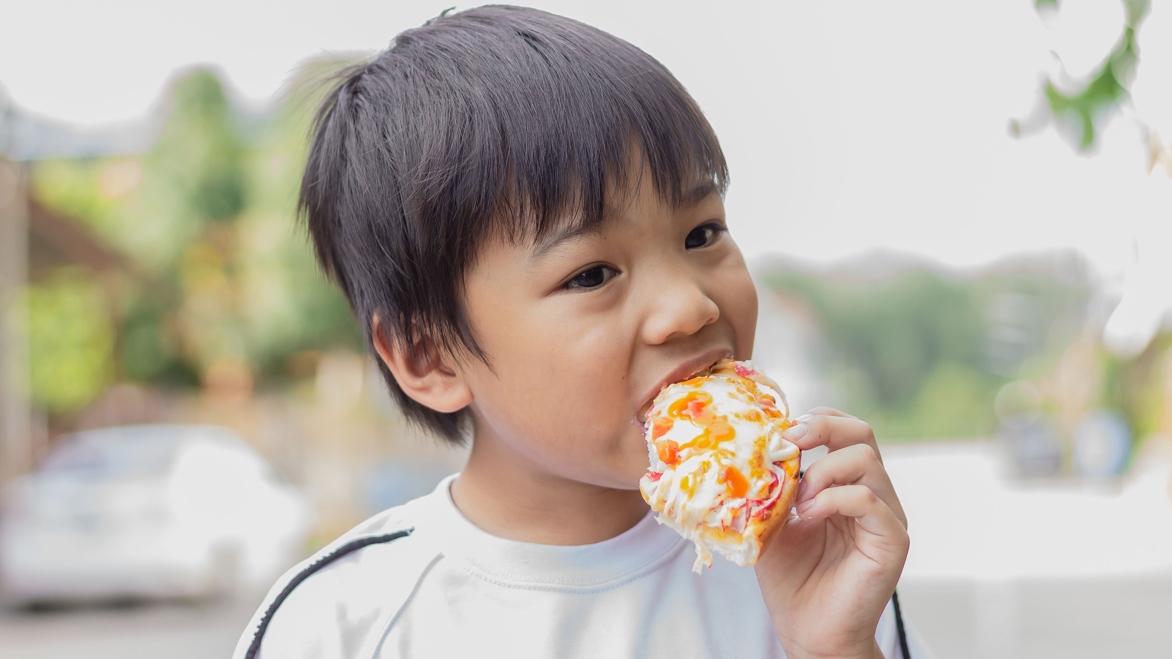 一個小男孩開心地咬著一片俗氣又五顏六色的pizza片 