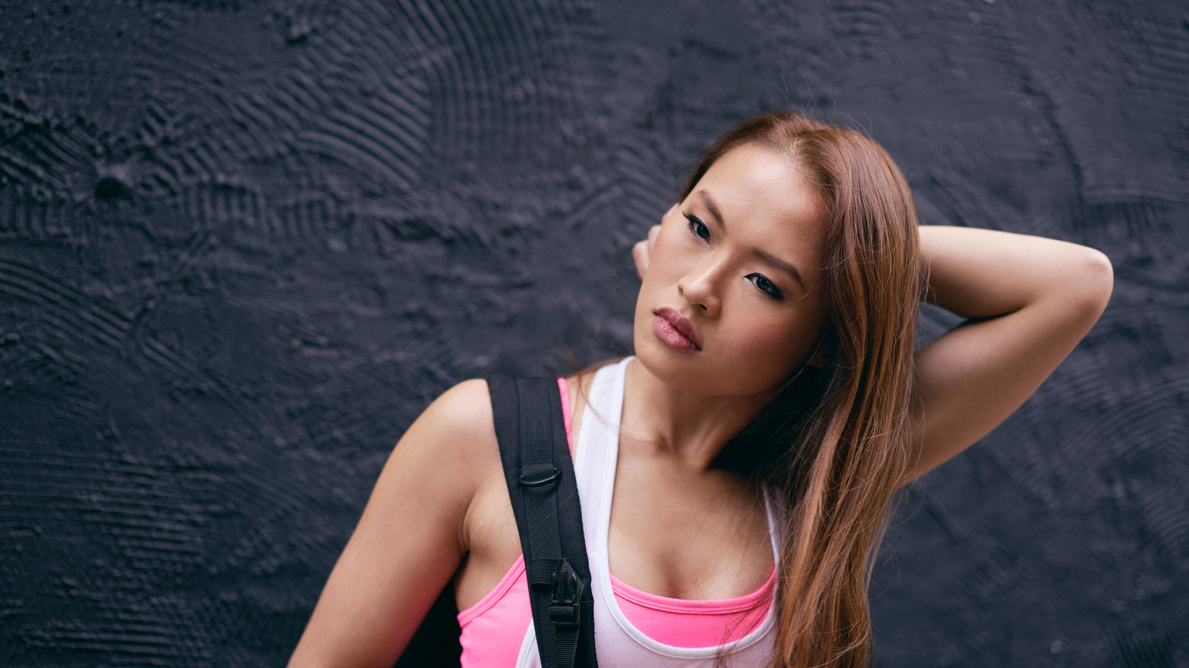 Portrait of beautiful young woman with hand in hair in front of black wall