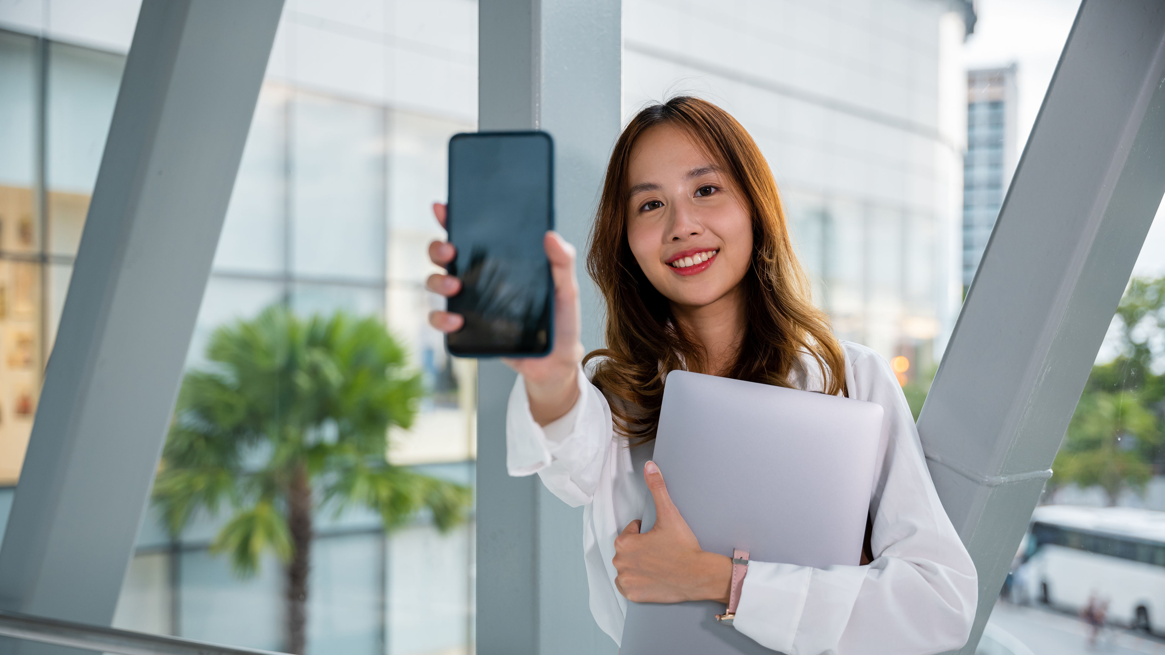 Productive woman in a white shirt multitasks with her laptop and phone in hand. 