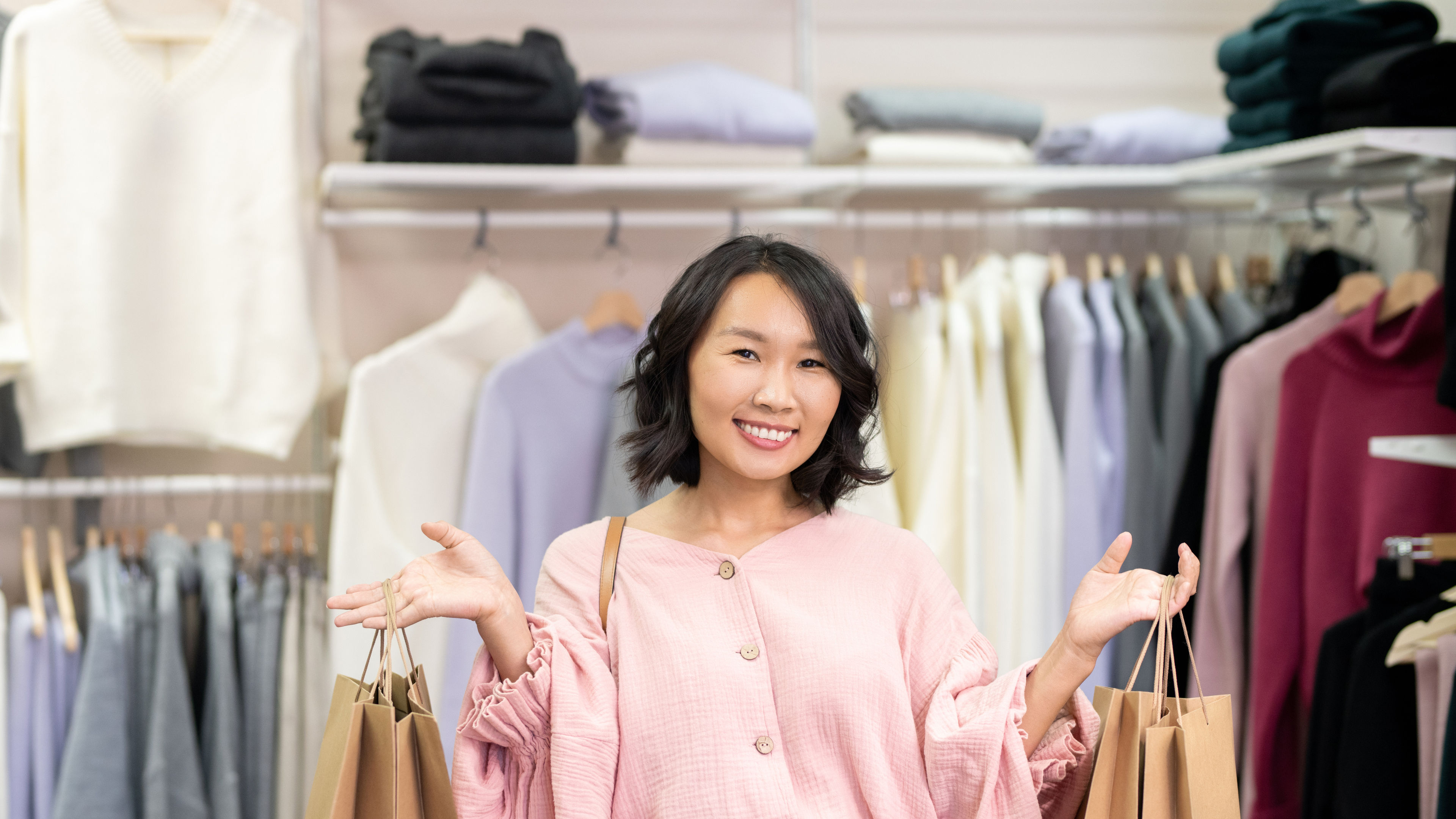 Young cheerful female shopaholic in smart casualwear holding big paperbags 