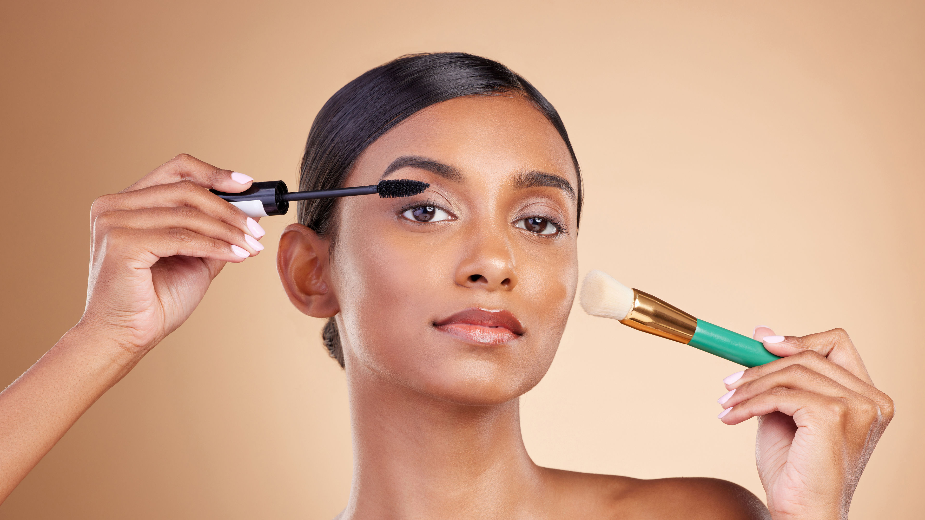 Indian women posing while applying mascara and makeup.