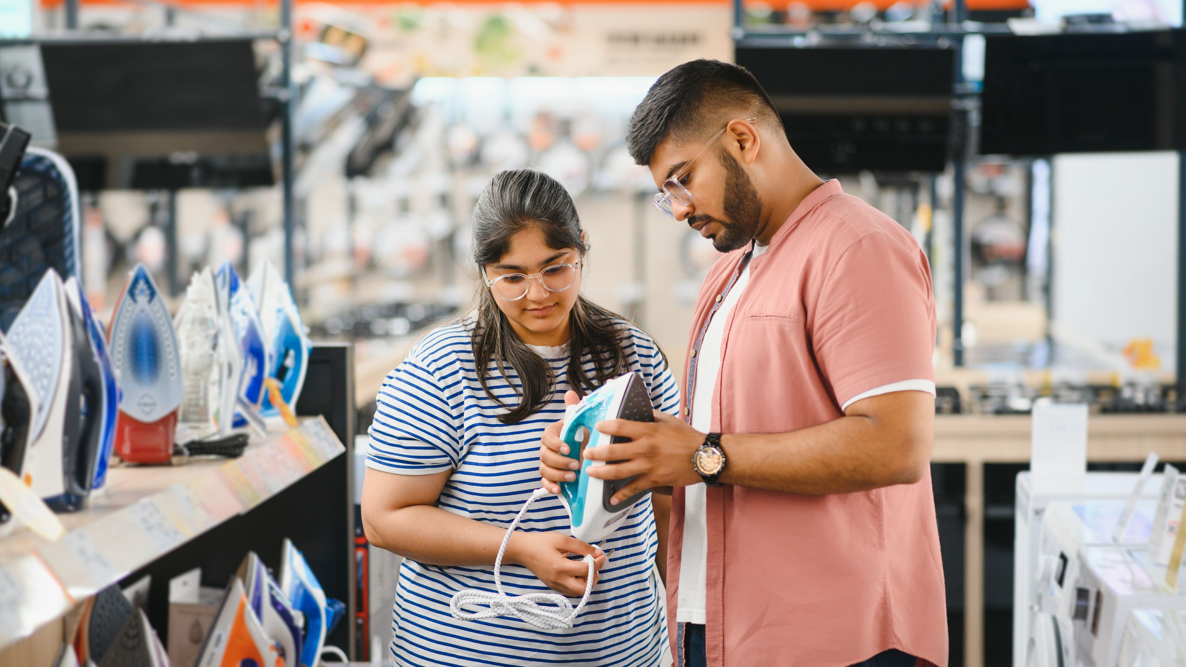 A couple stands in an electronics store, carefully choosing an electric iron 
