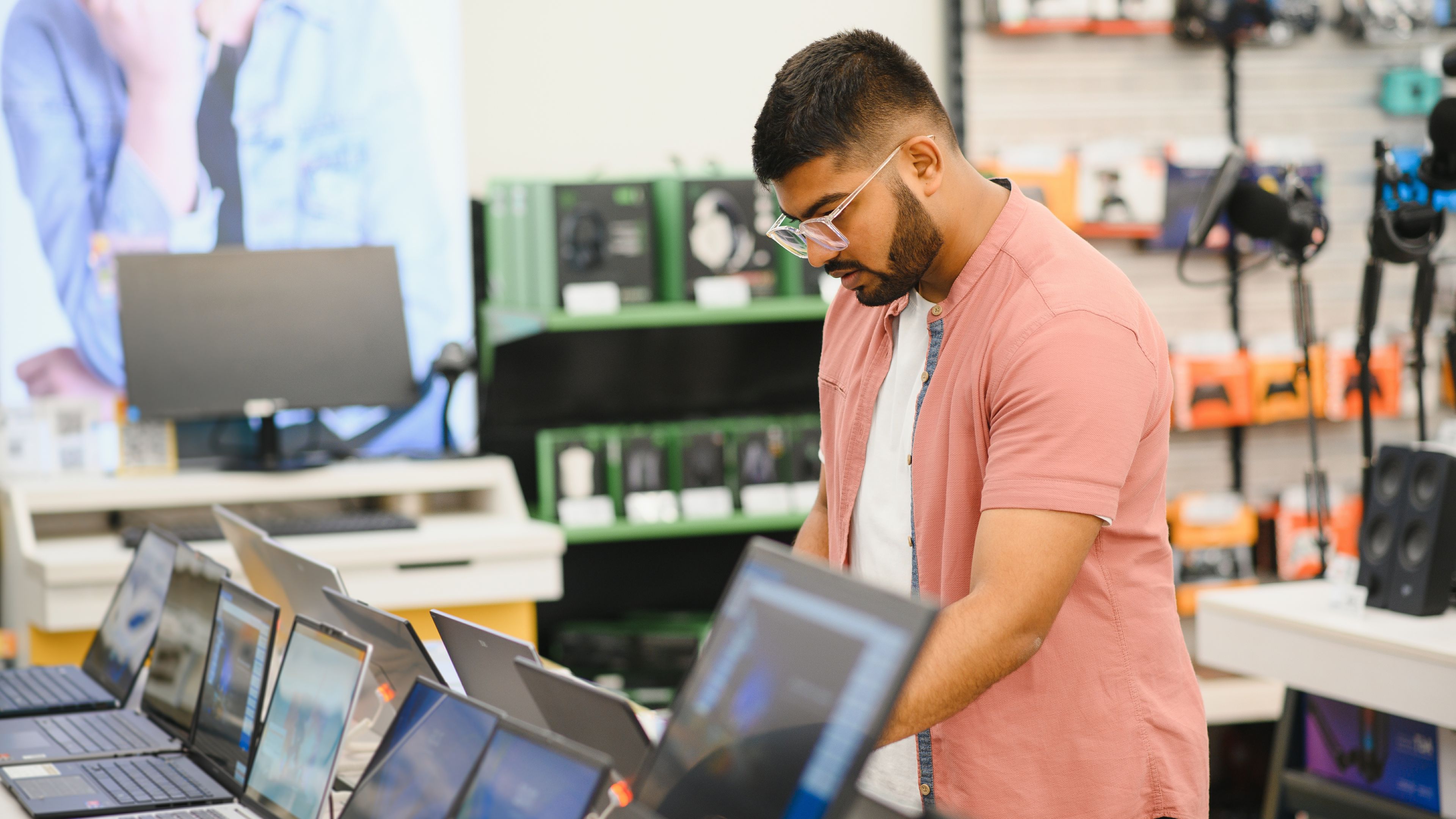 A young man stands behind his laptop at the electronics store