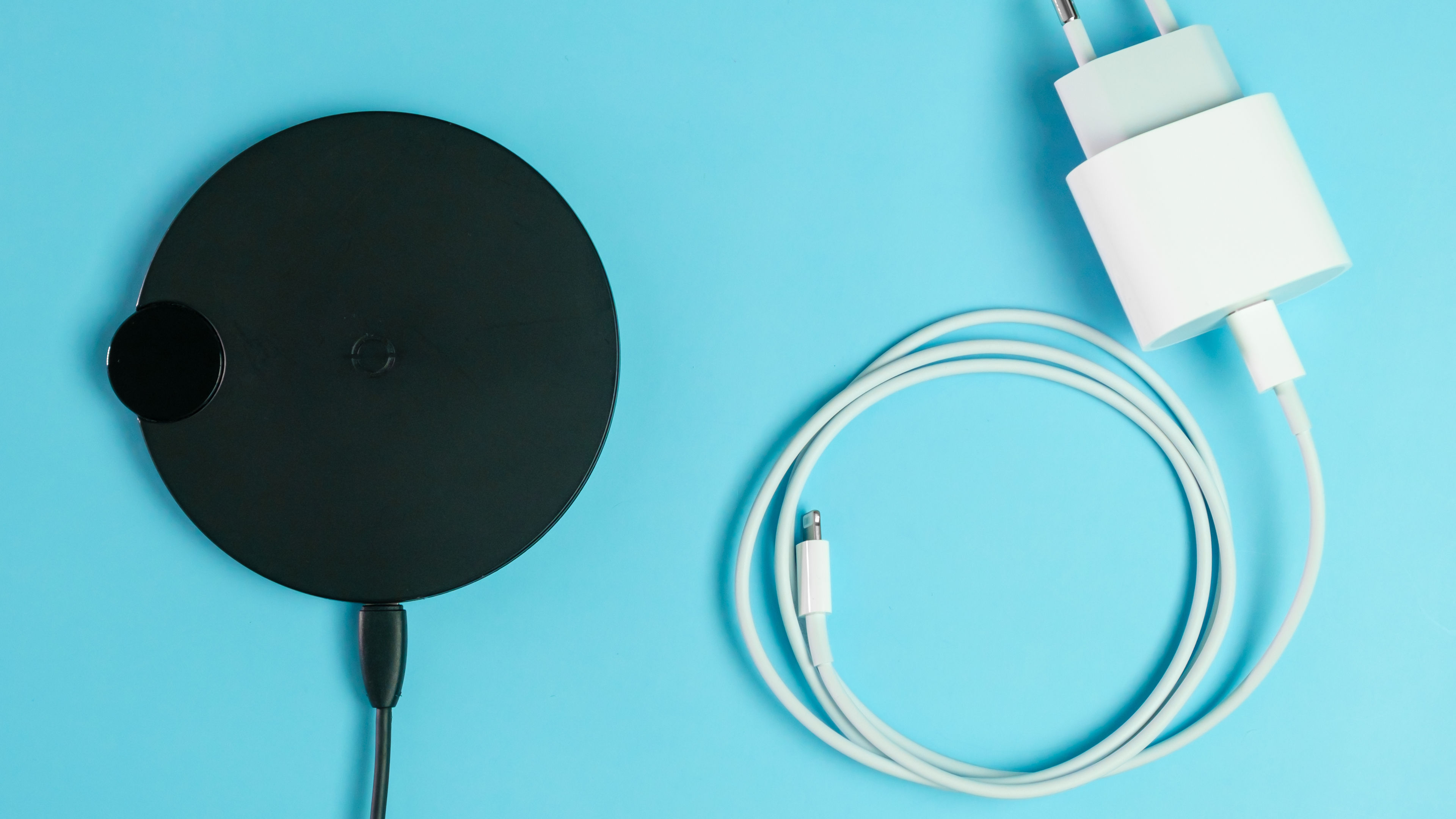 Black wireless charger vs a white lightning USB A cable on the blue background