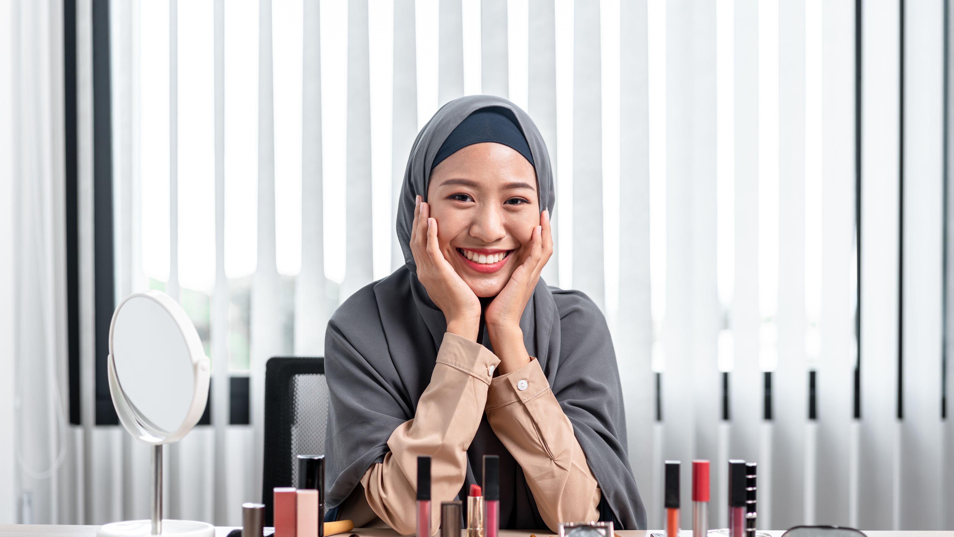 Potret wanita Muslim Asia melihat kamera dan tersenyum dengan mengajar tutorial solek dalam talian secara langsung. 