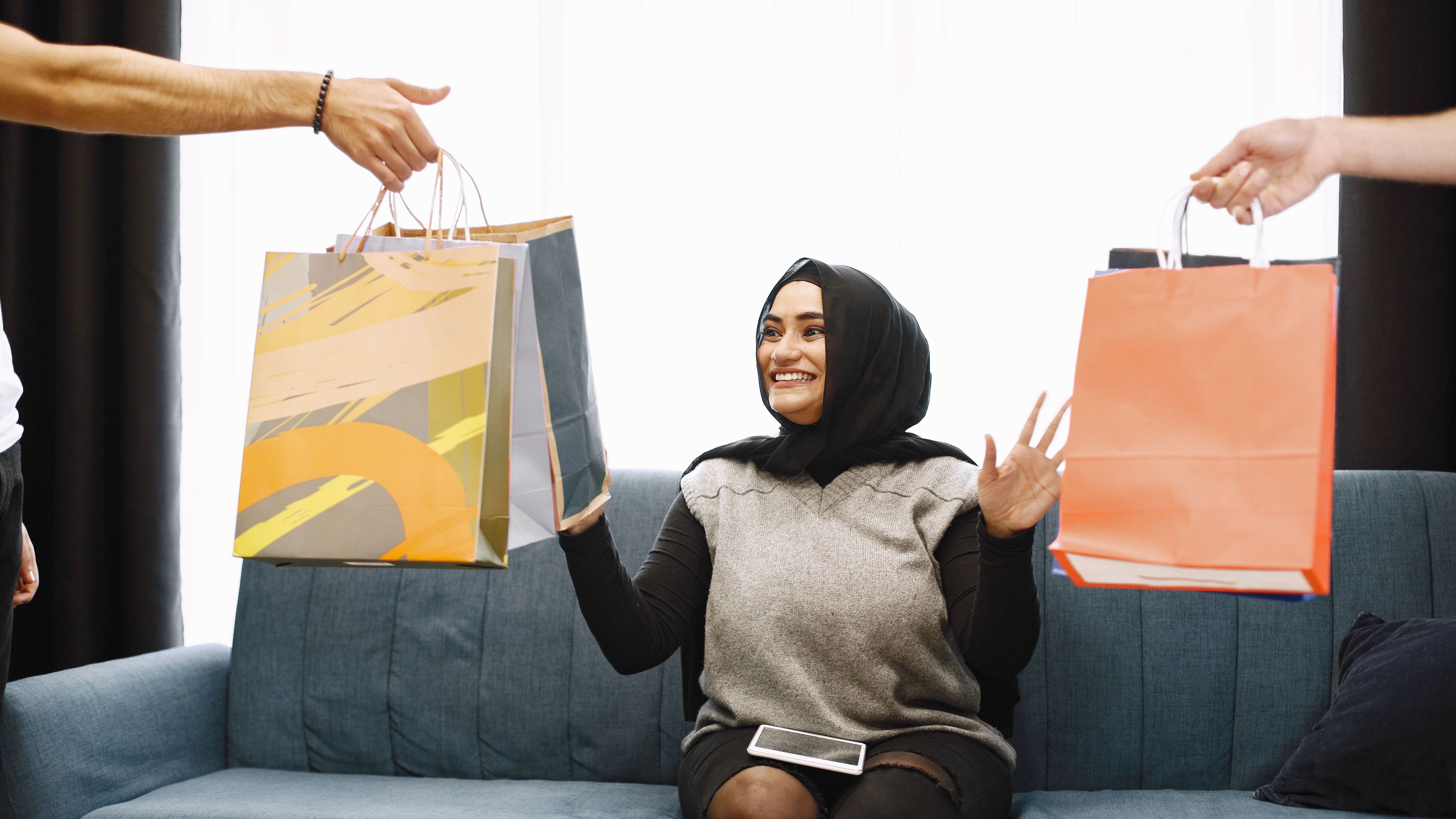 امرأة عربية ترتدي الحجاب تجلس على أريكة سوداء في المنزل ، تقوم بالتسوق عبر الإنترنت.