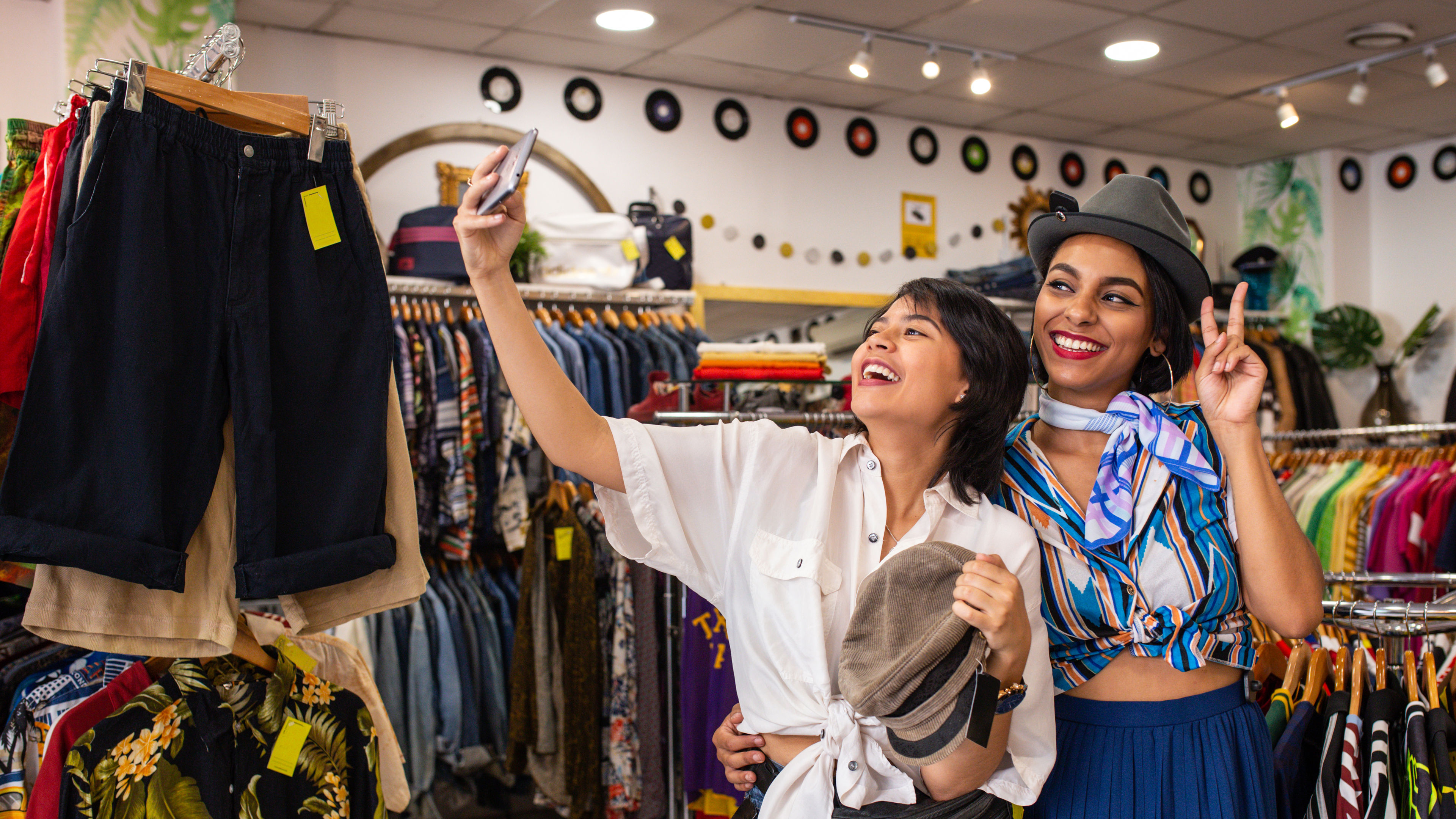 Cheerful friends trying on hats in the shop and taking selfies 