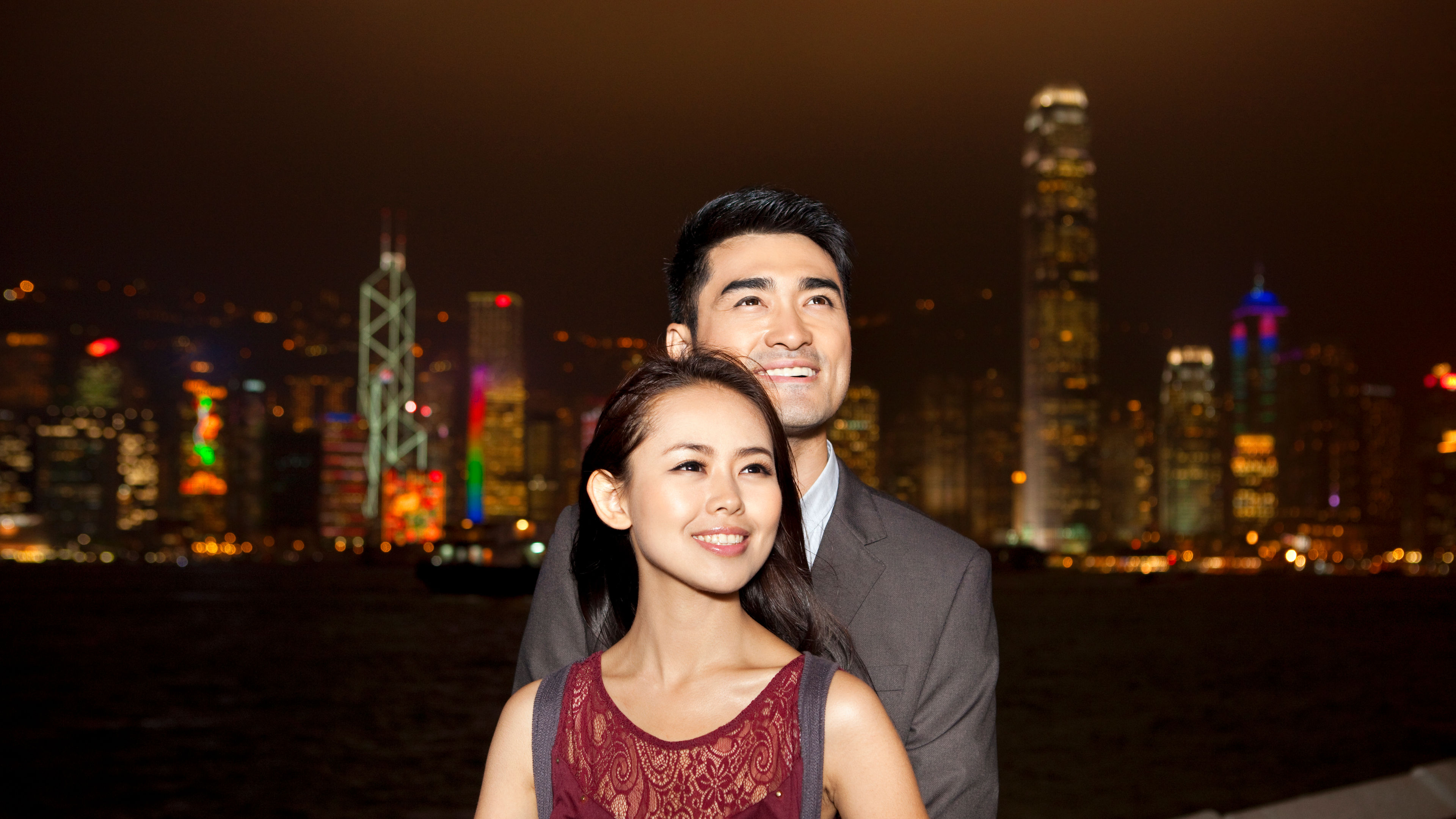 Happy young couple enjoying the night view of Victoria Harbor, Hong Kong 
