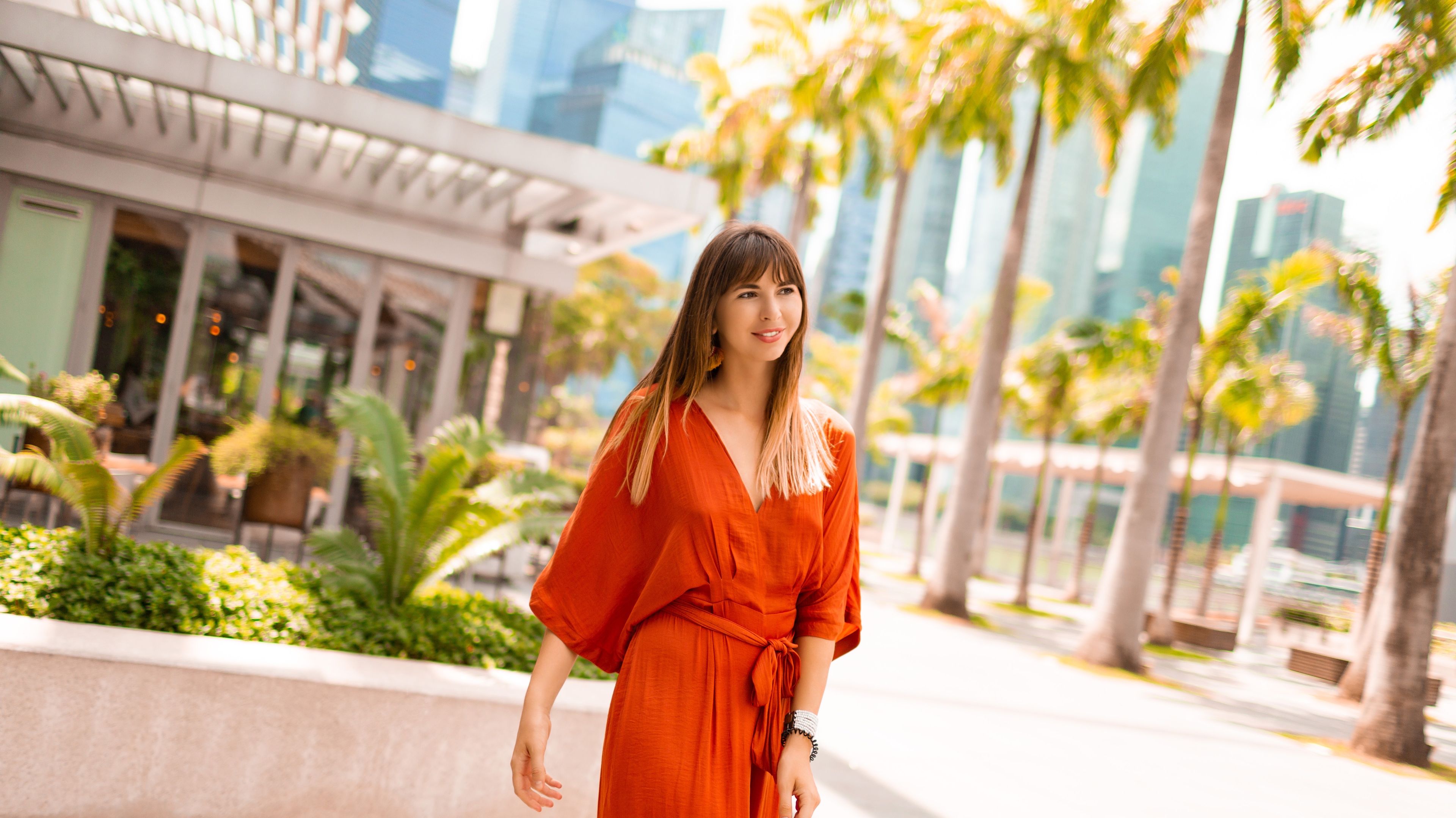 Stylish woman in orange dress posing on promenade with palm trees 
