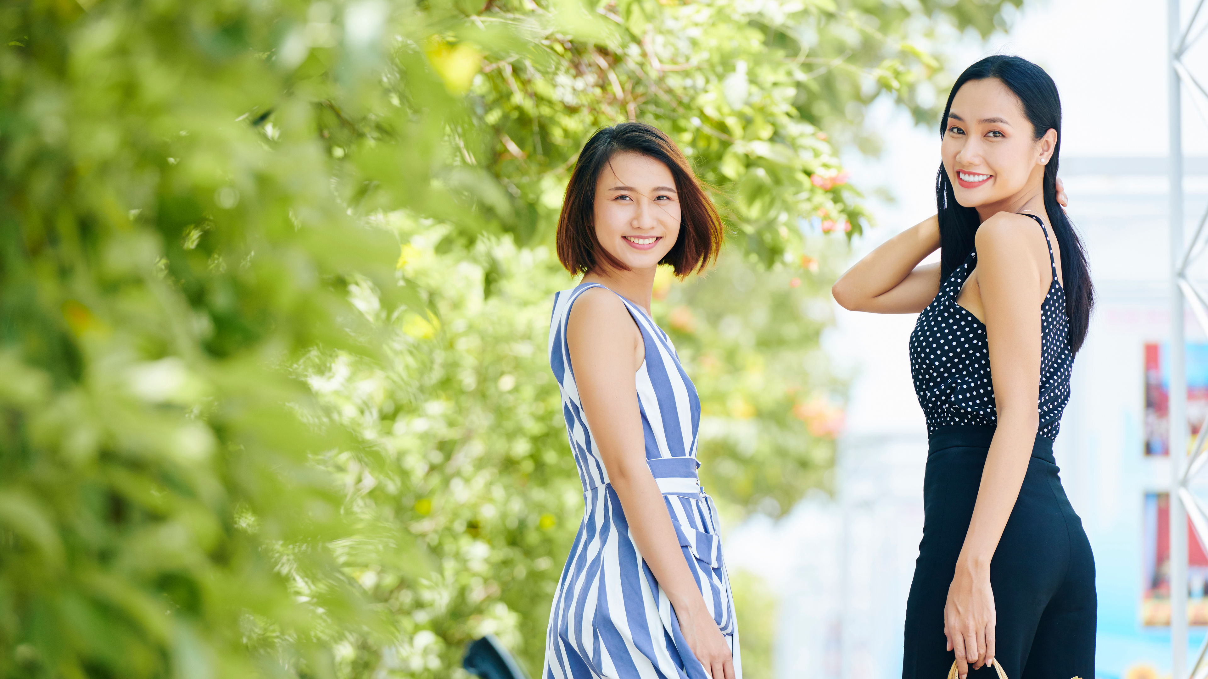 Portrait of two Asian women looking very stylish smiling at camera while walking along the street in the city 
