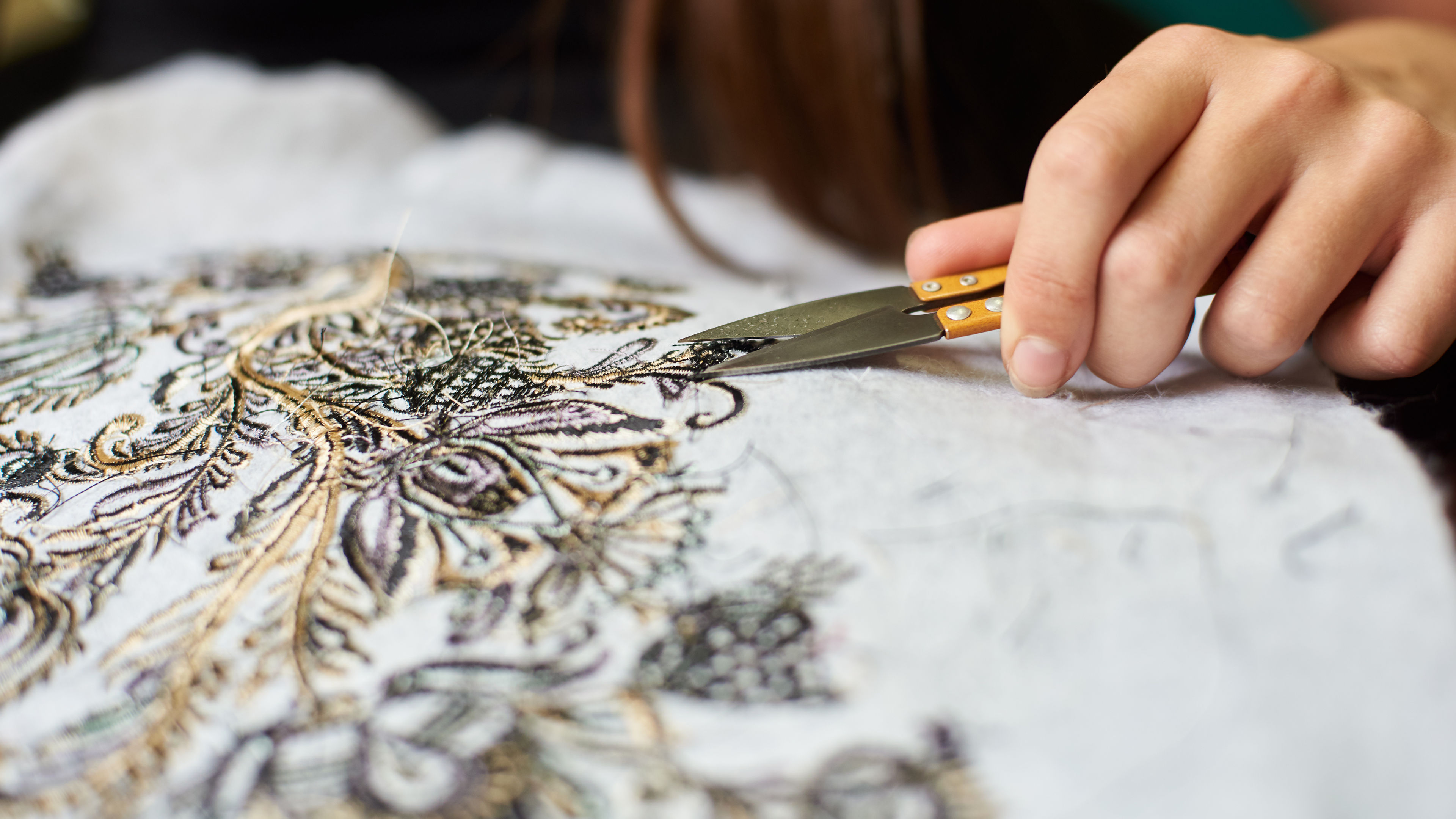 Woman hands cutting away loose ends of threads from fabric with machine embroidery using scissors