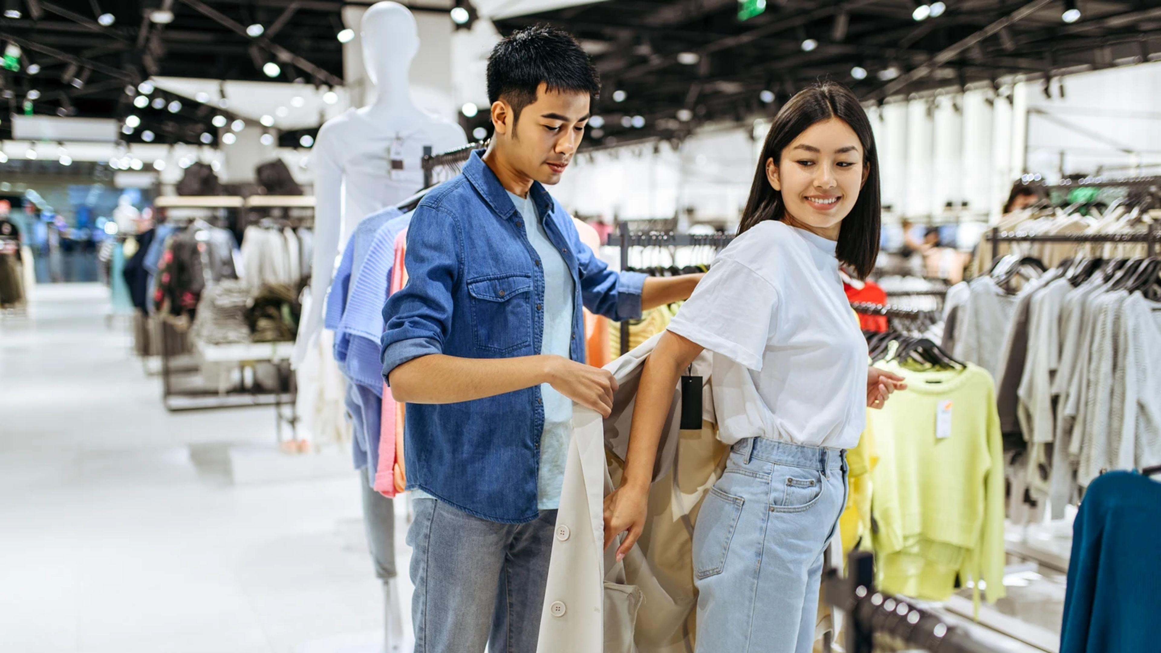 Asian man helping his girlfriend to wear a new dress from the clothing store.
