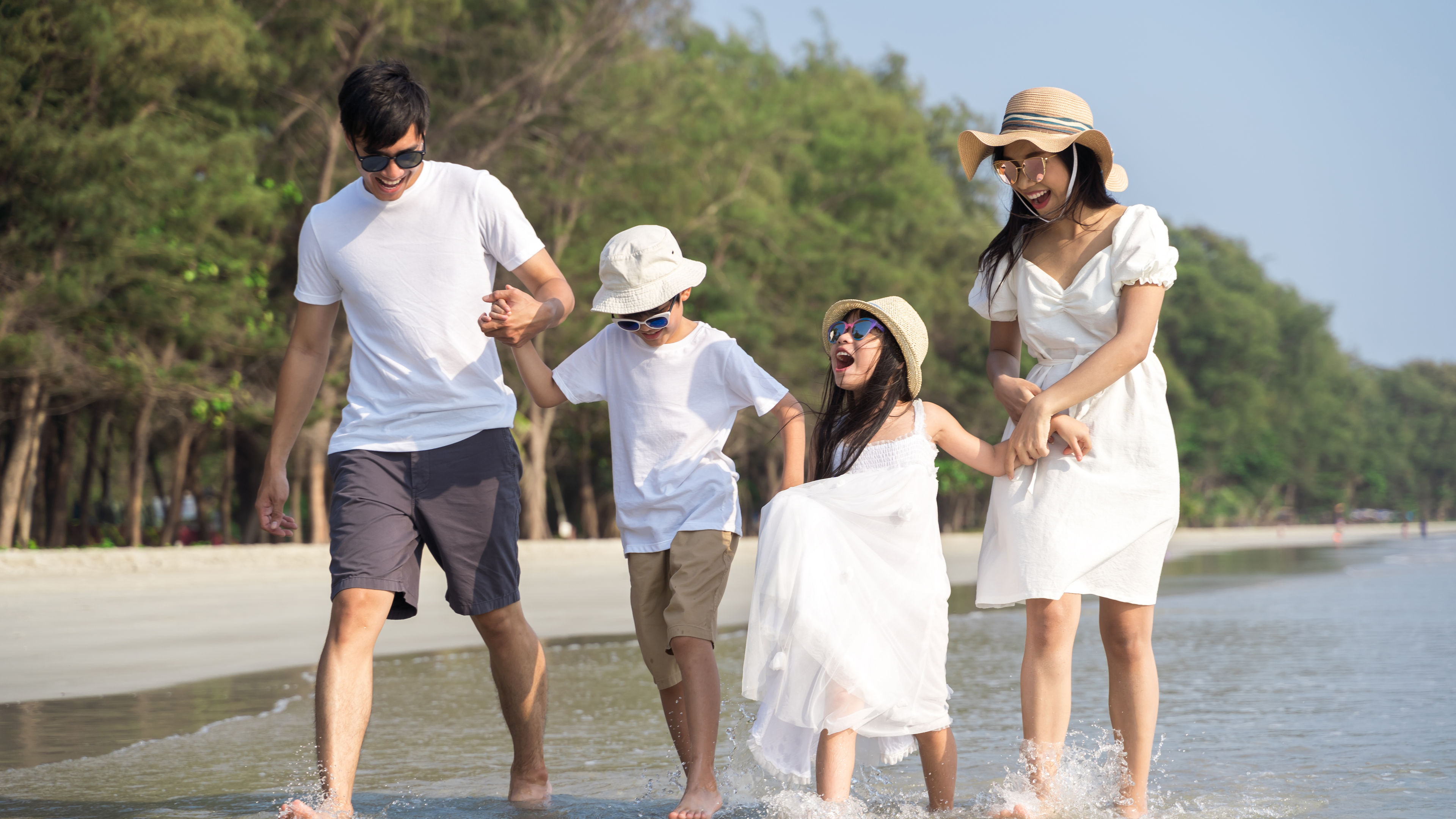 Beyazlar içinde mutlu bir aile, bir plajda yürüyor.