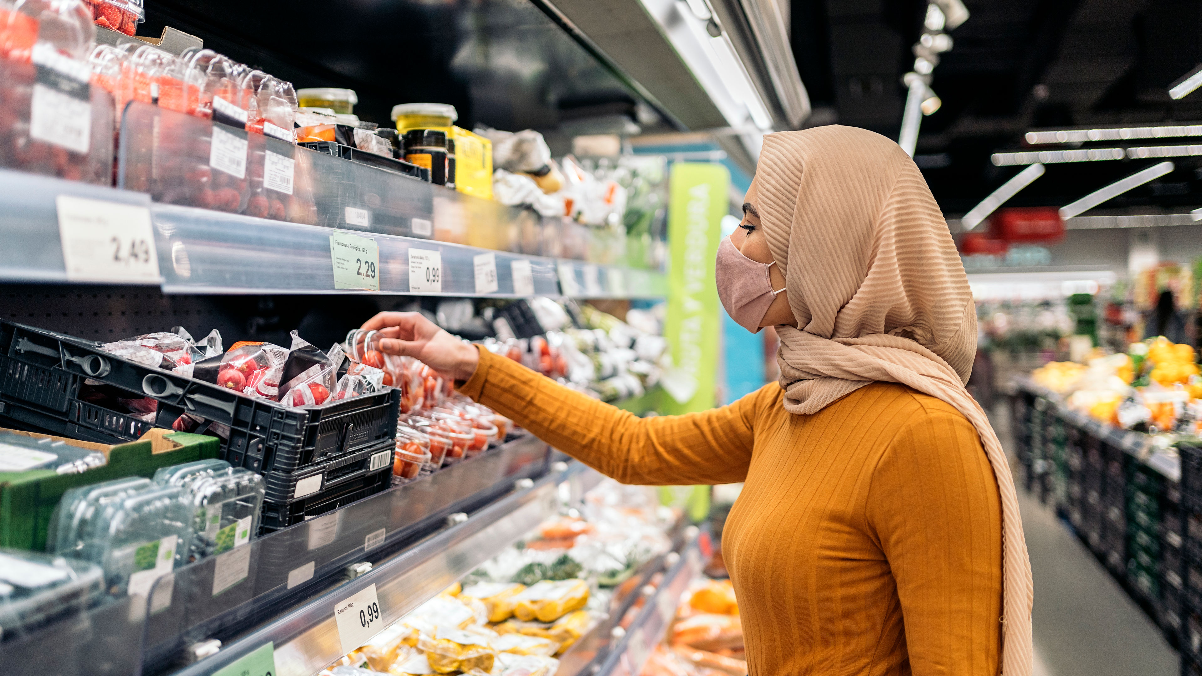 Young muslim woman wearing protective face mask buying in the groceries shop. 
