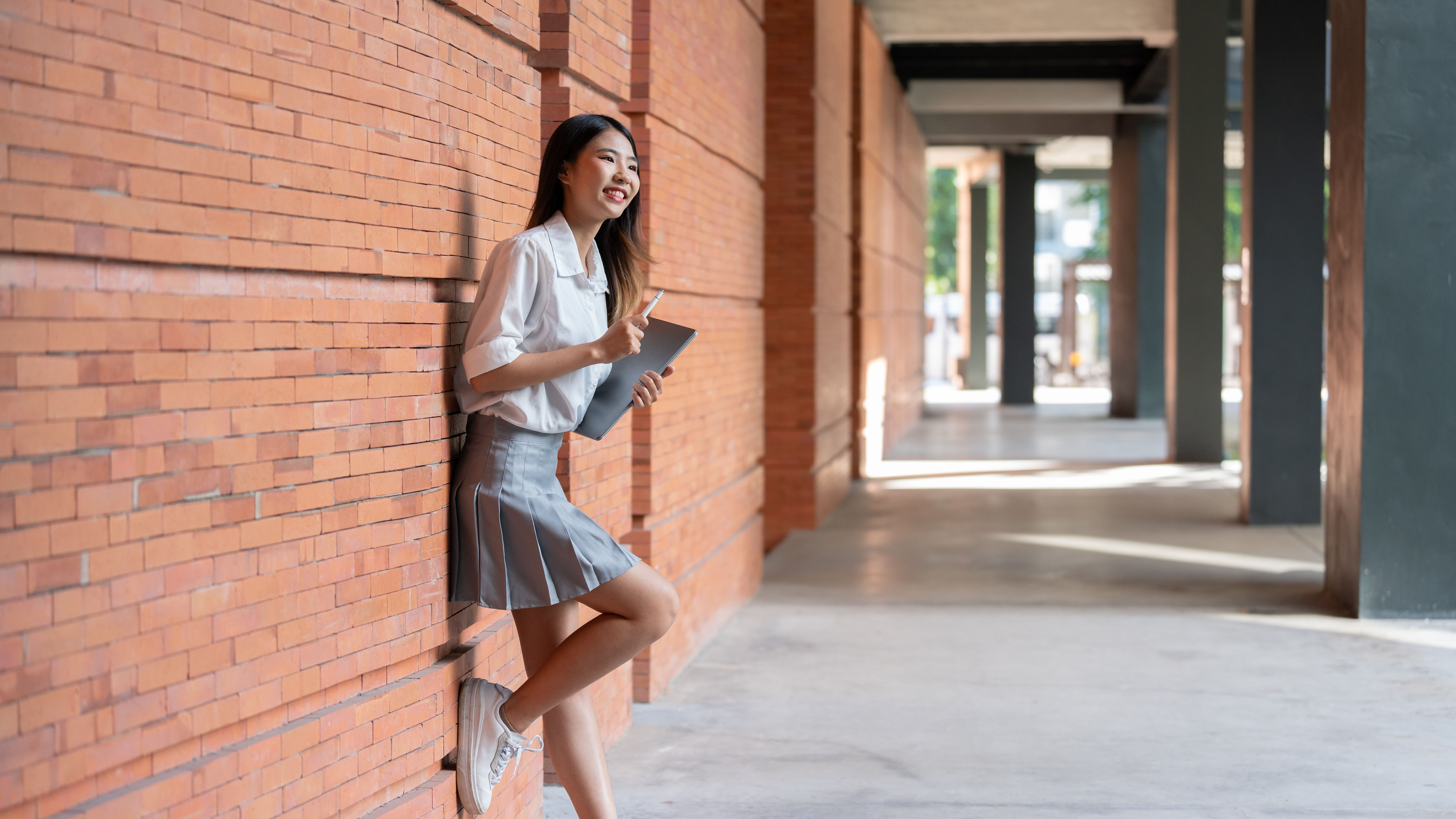 A young woman is standing and leaning against a brick wall