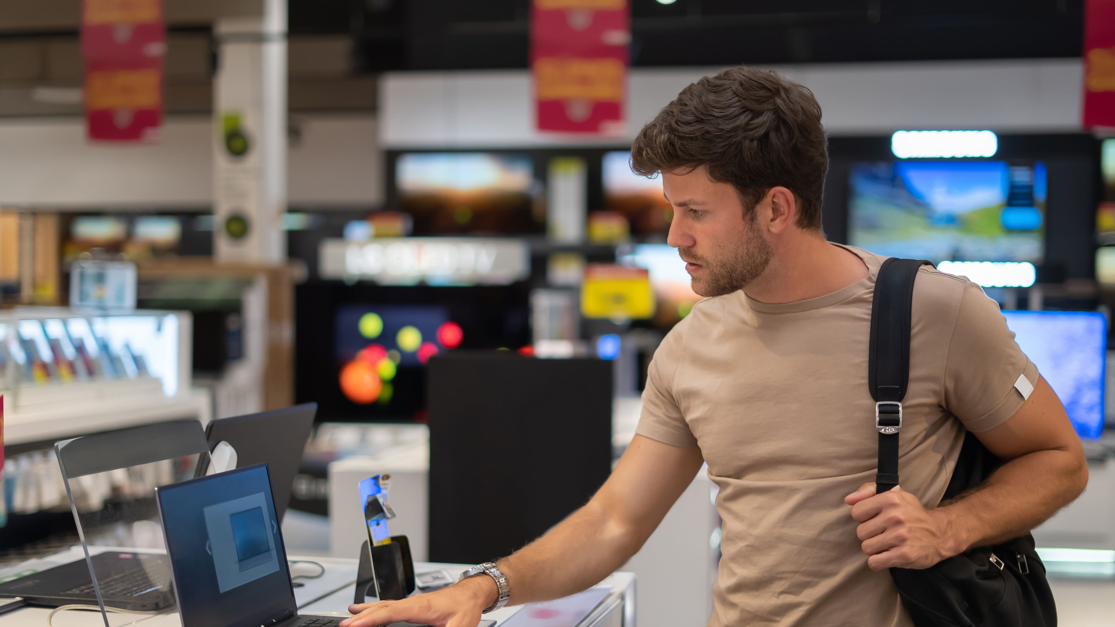 A man is carefully inspecting a new netbook in an electronics store during a shopping visit 