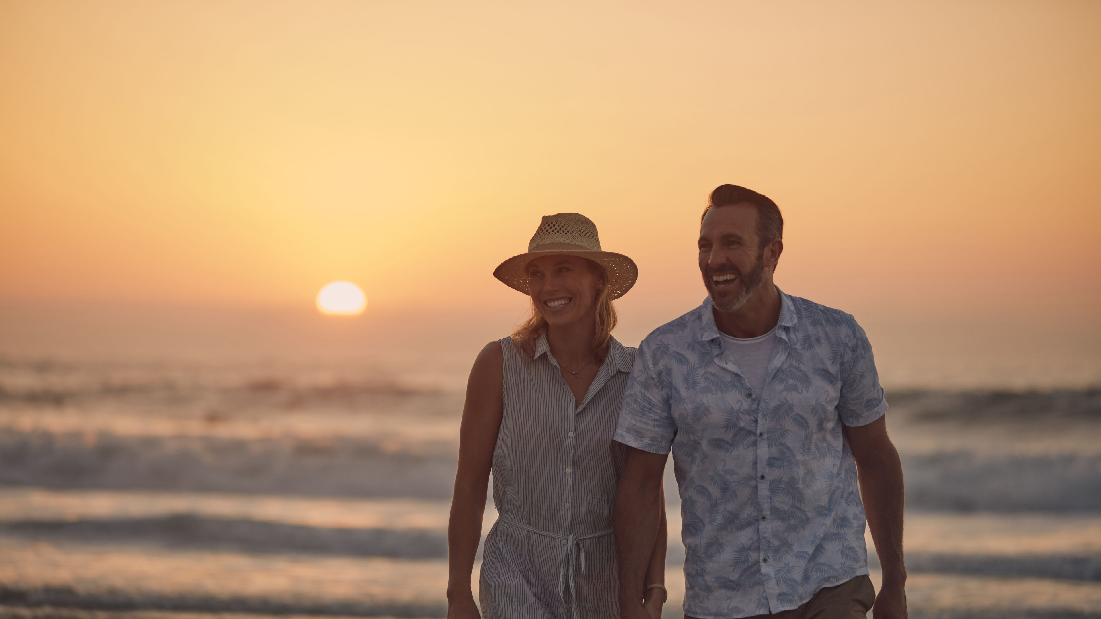A smiling couple holding hands while walking along the shoreline