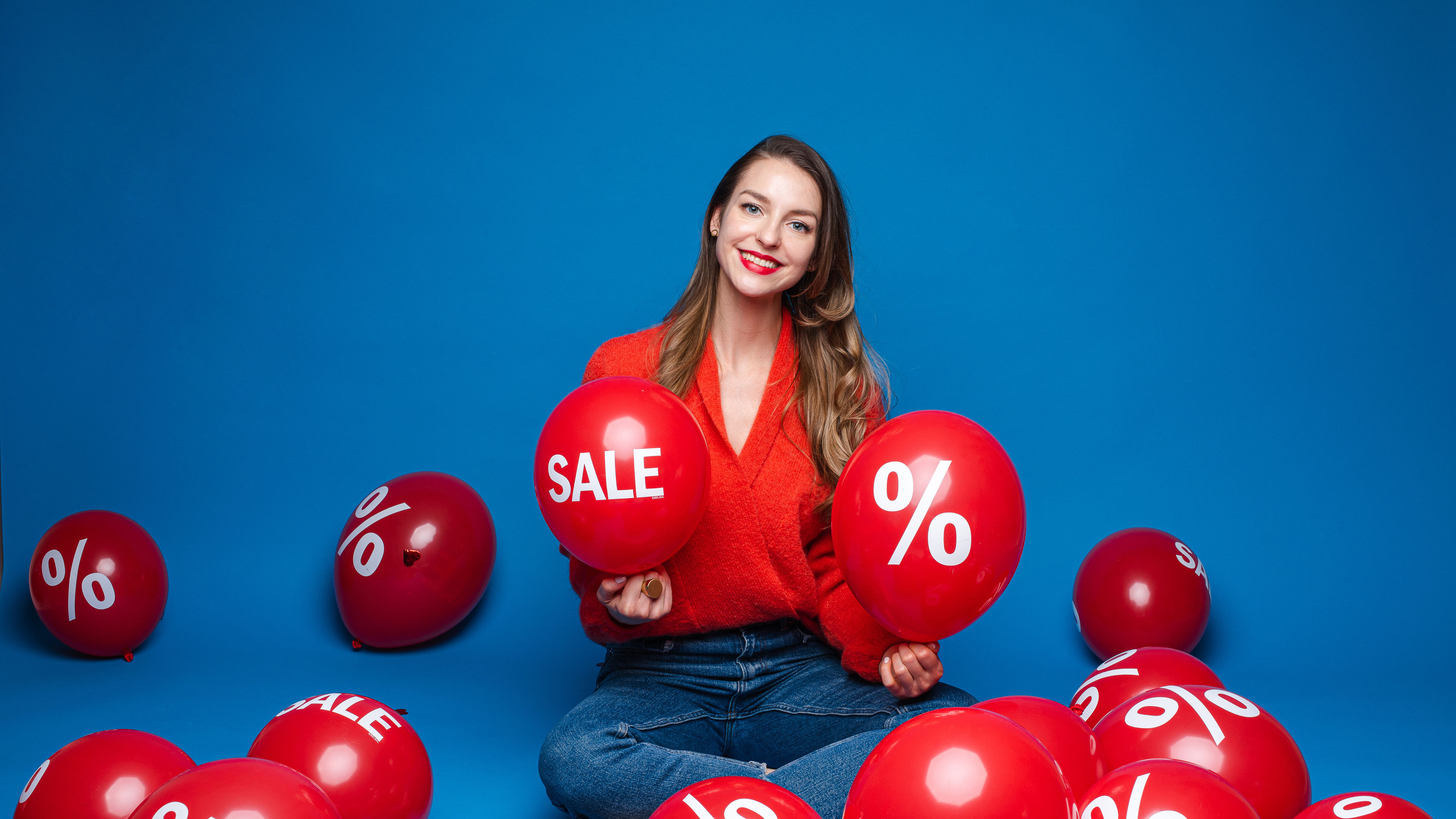 beautiful female model poses for the camera with a lot of red air baloons 