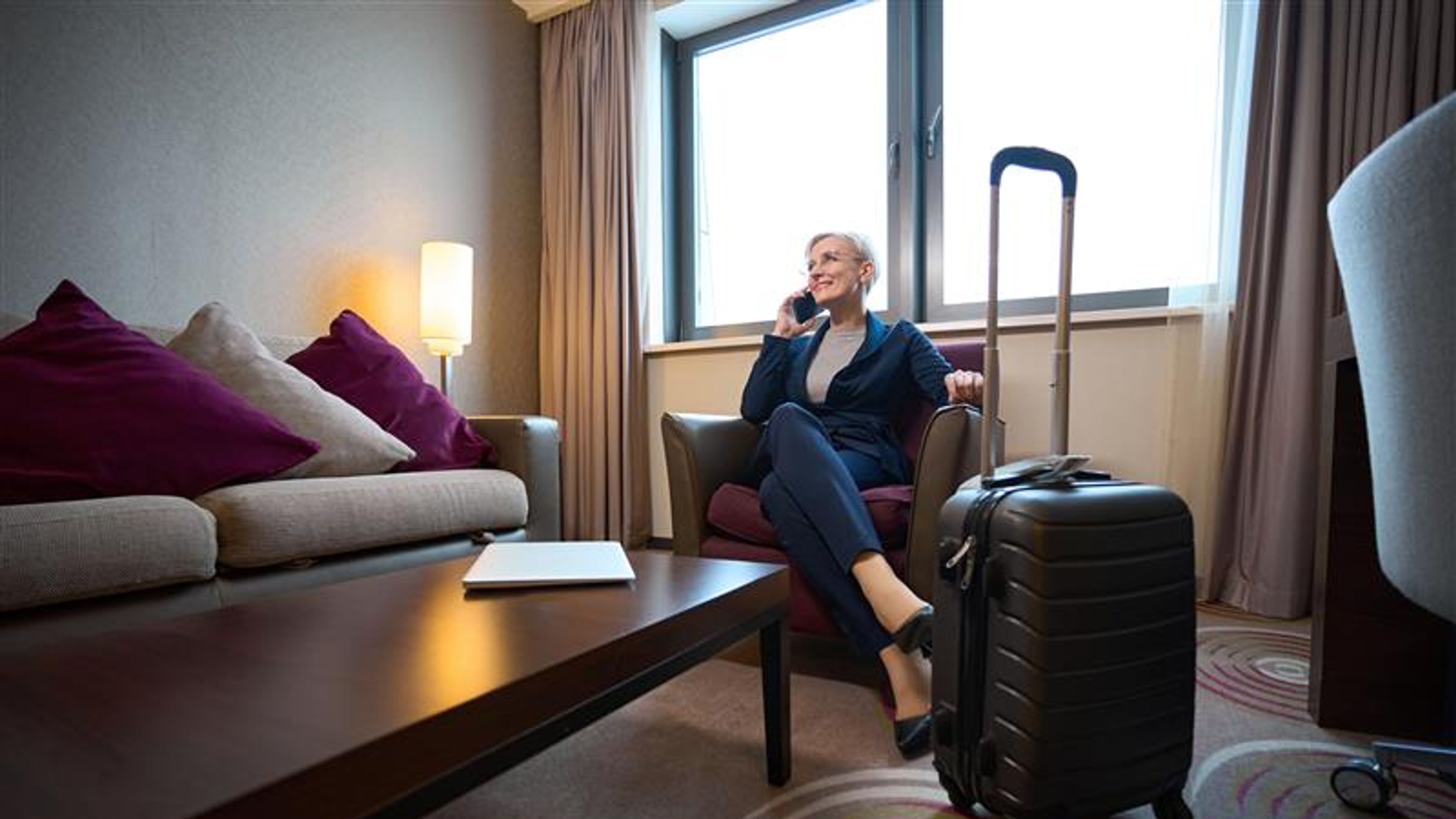 Businesswoman talking on smartphone in armchair in hotel room 