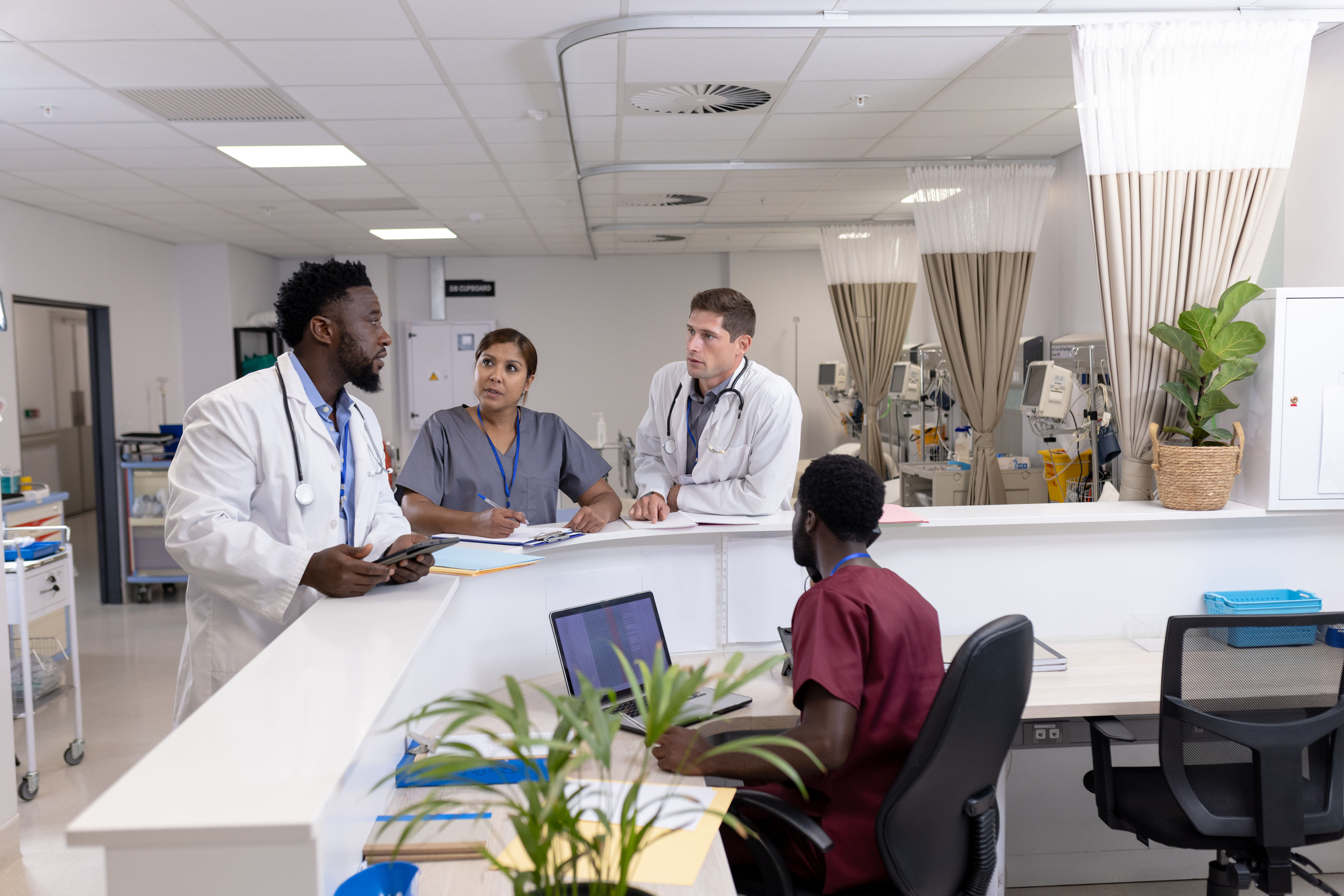 Diverse doctors and medical staff talking at reception desk of hospital ward 