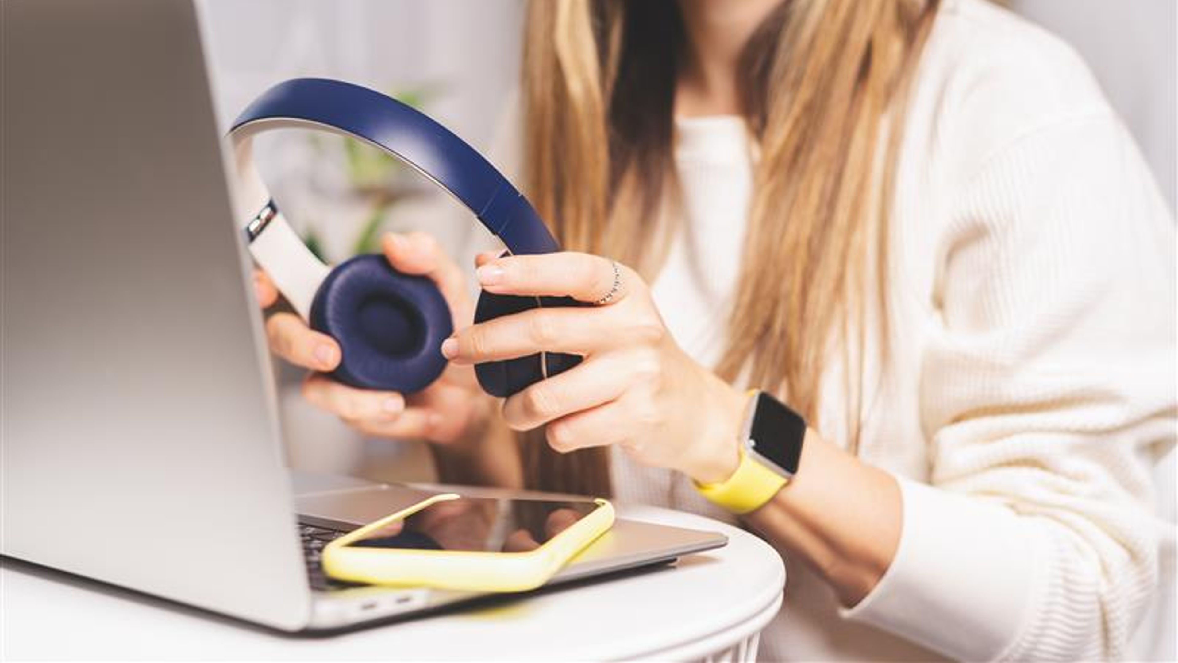 Freelance woman with headphones and laptop listening to music, texting at mobile cell phone and online shopping at home.