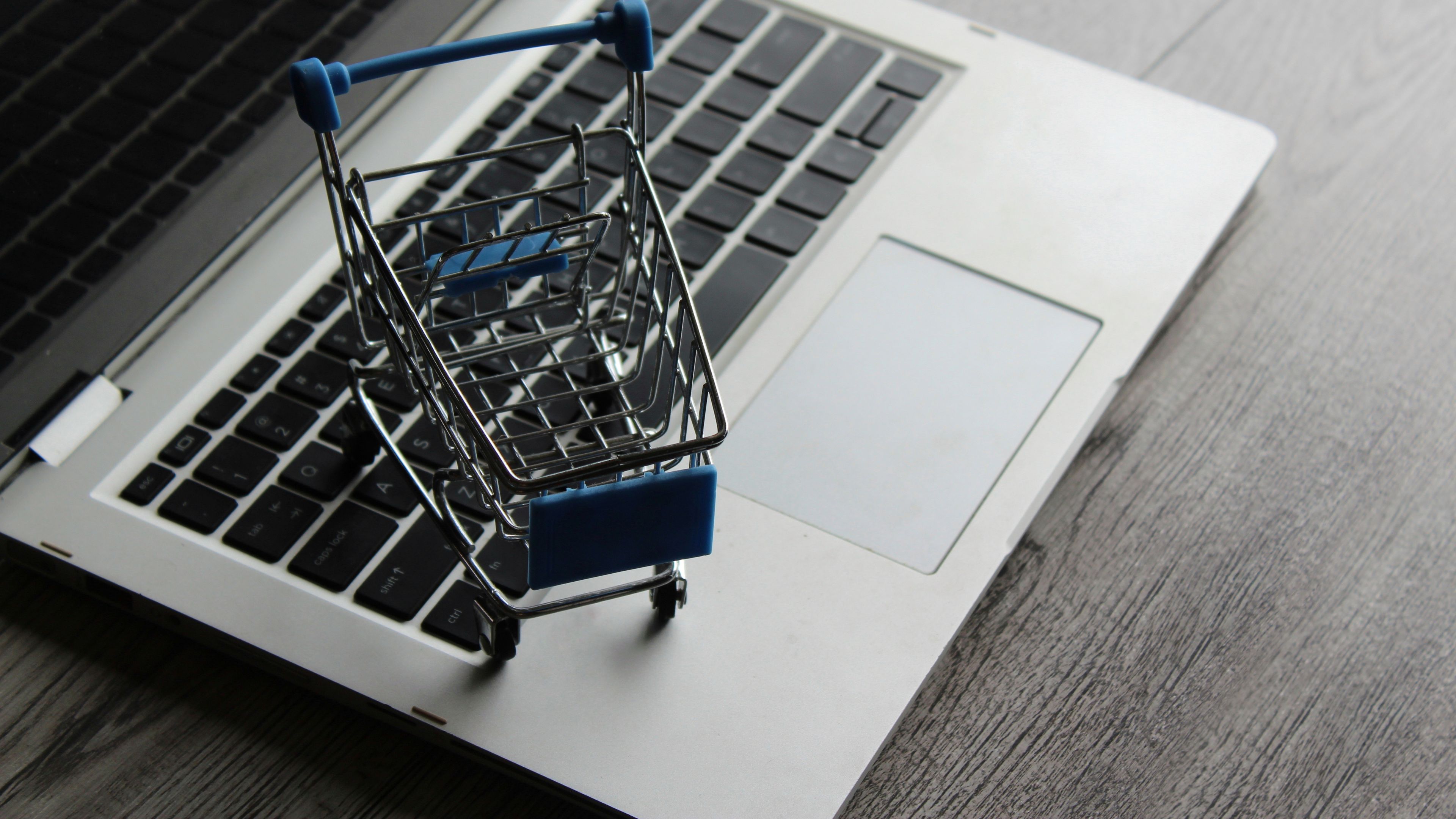 A small metallic shopping cart sitting on the keyboard of a laptop 