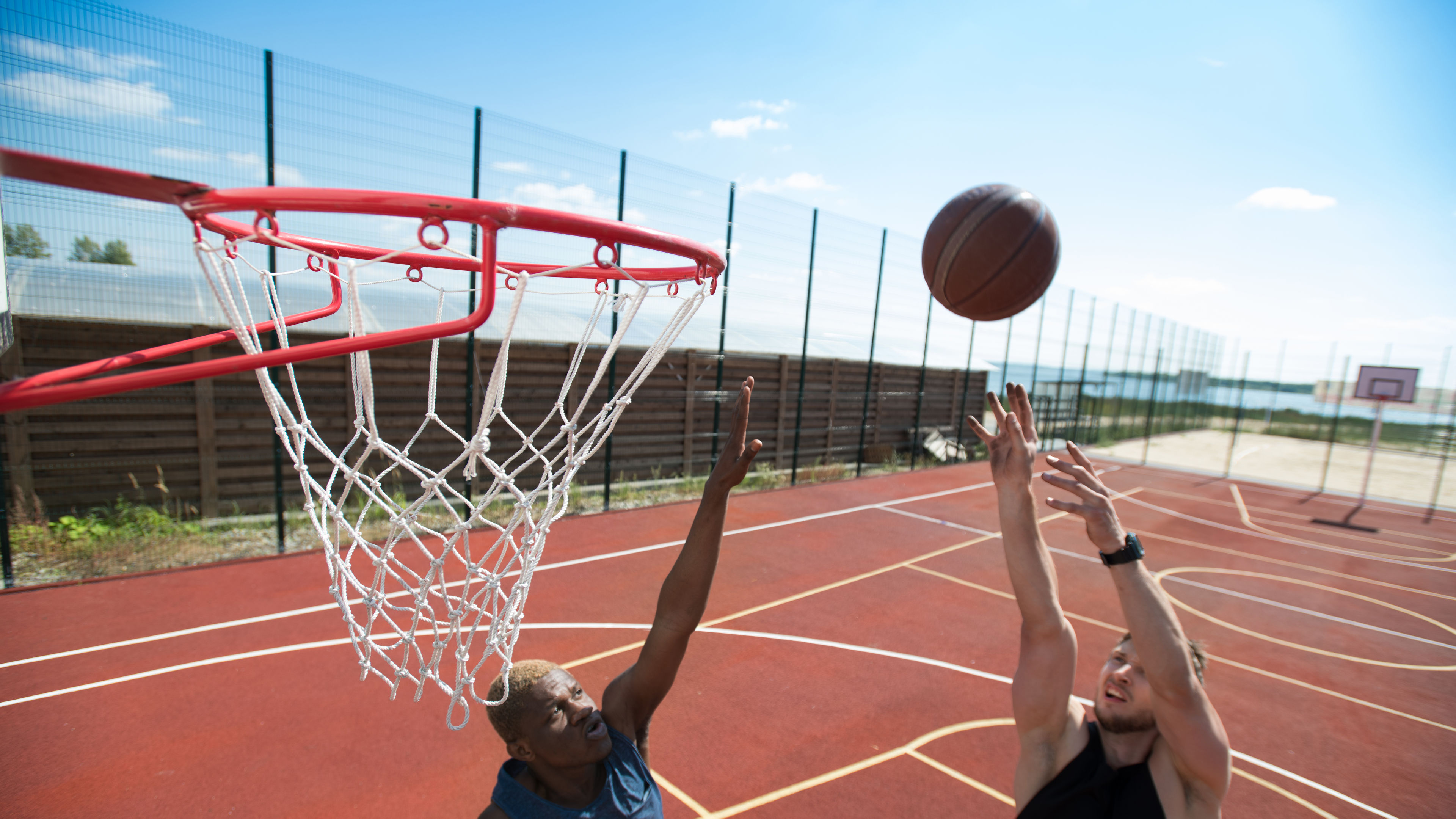 Portrait of young basketball player throwing ball in basket on outdoor court lit by sunlight, copy space 