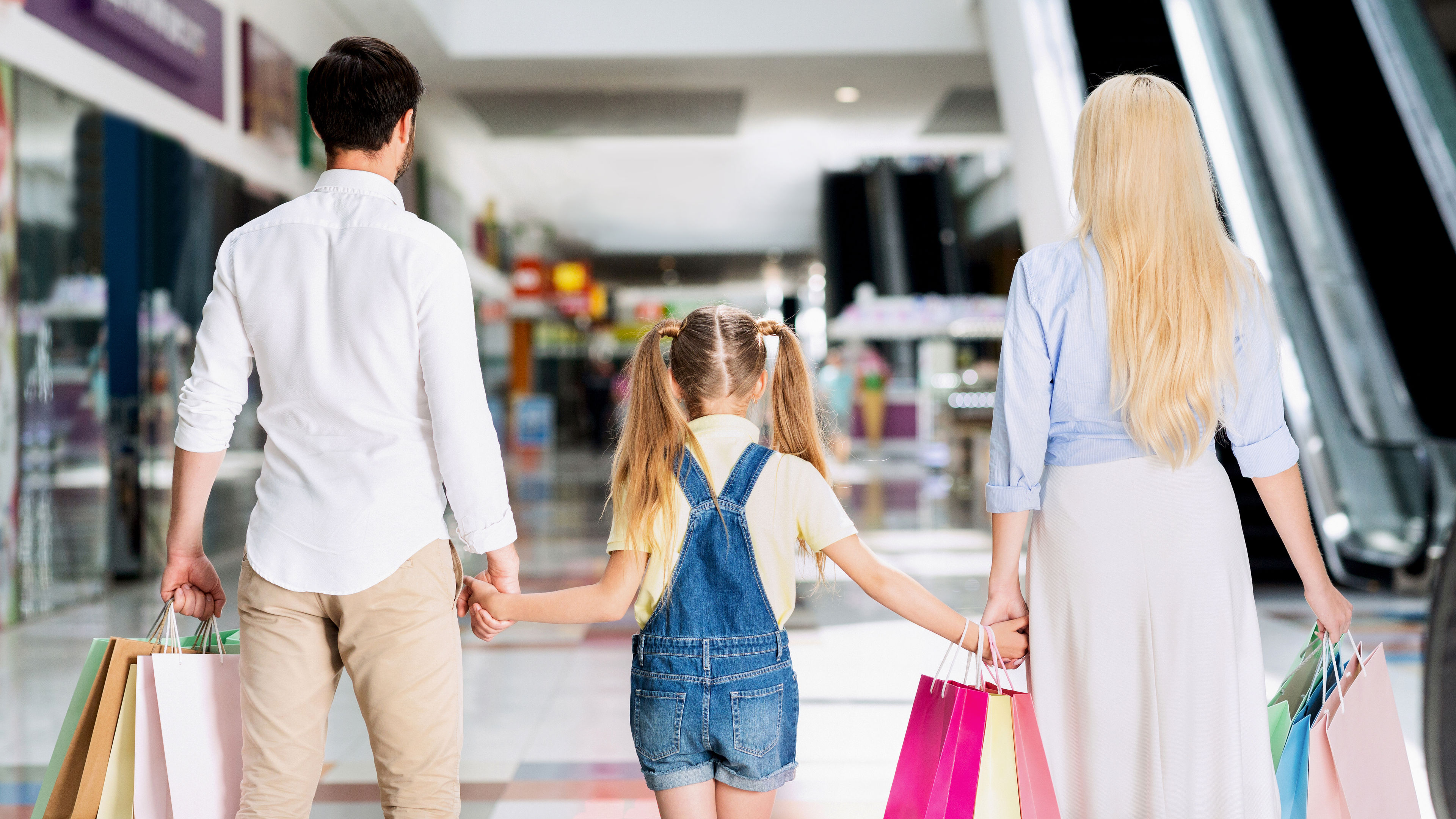 Unrecognizable Parents And Daughter Walking In Shopping Mall, Back View 